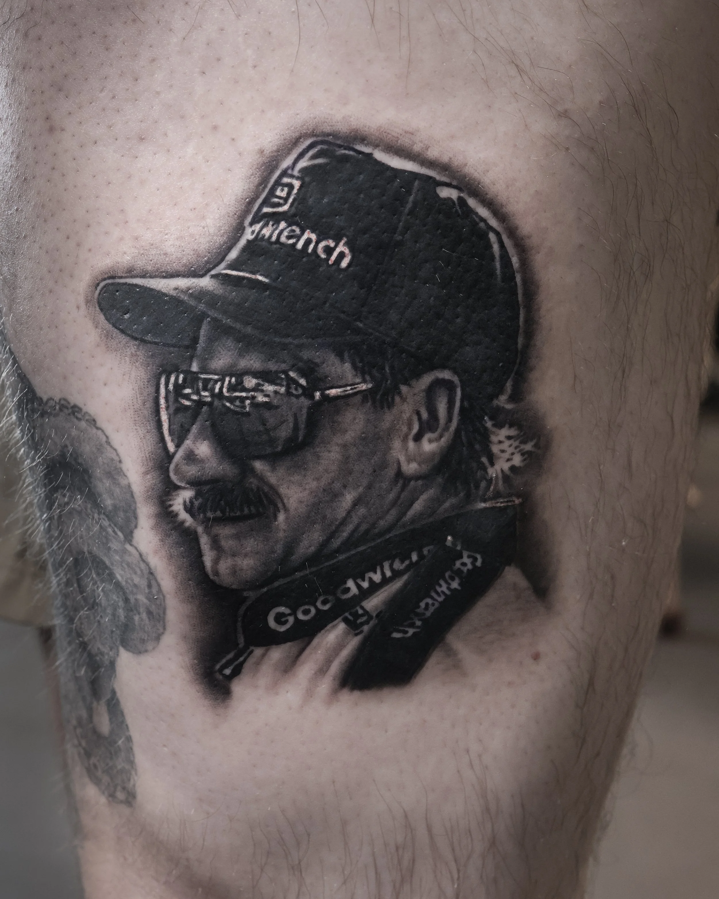 Close-up of a tattoo on a person's face depicting a man with a beard wearing a hat that says 'Goorich'.