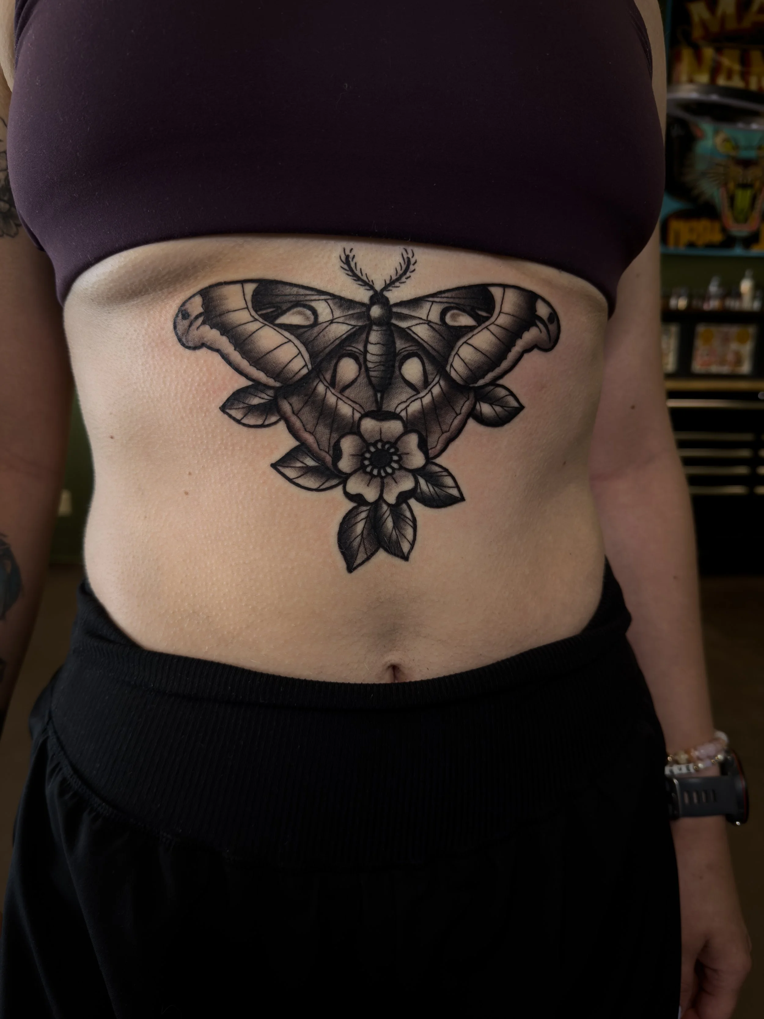 Tattoo of a moth with a flower below it on a person's lower abdomen.