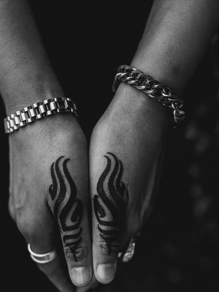 Two hands with tattoos on the fingers, wearing metal bracelets and rings, captured in black and white.