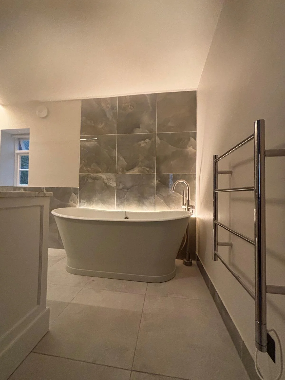 A modern bathroom featuring a freestanding bathtub, a walk-in glass shower with a rain showerhead, a marble vanity with a sink, and checkered floor tiles with a small trash bin.