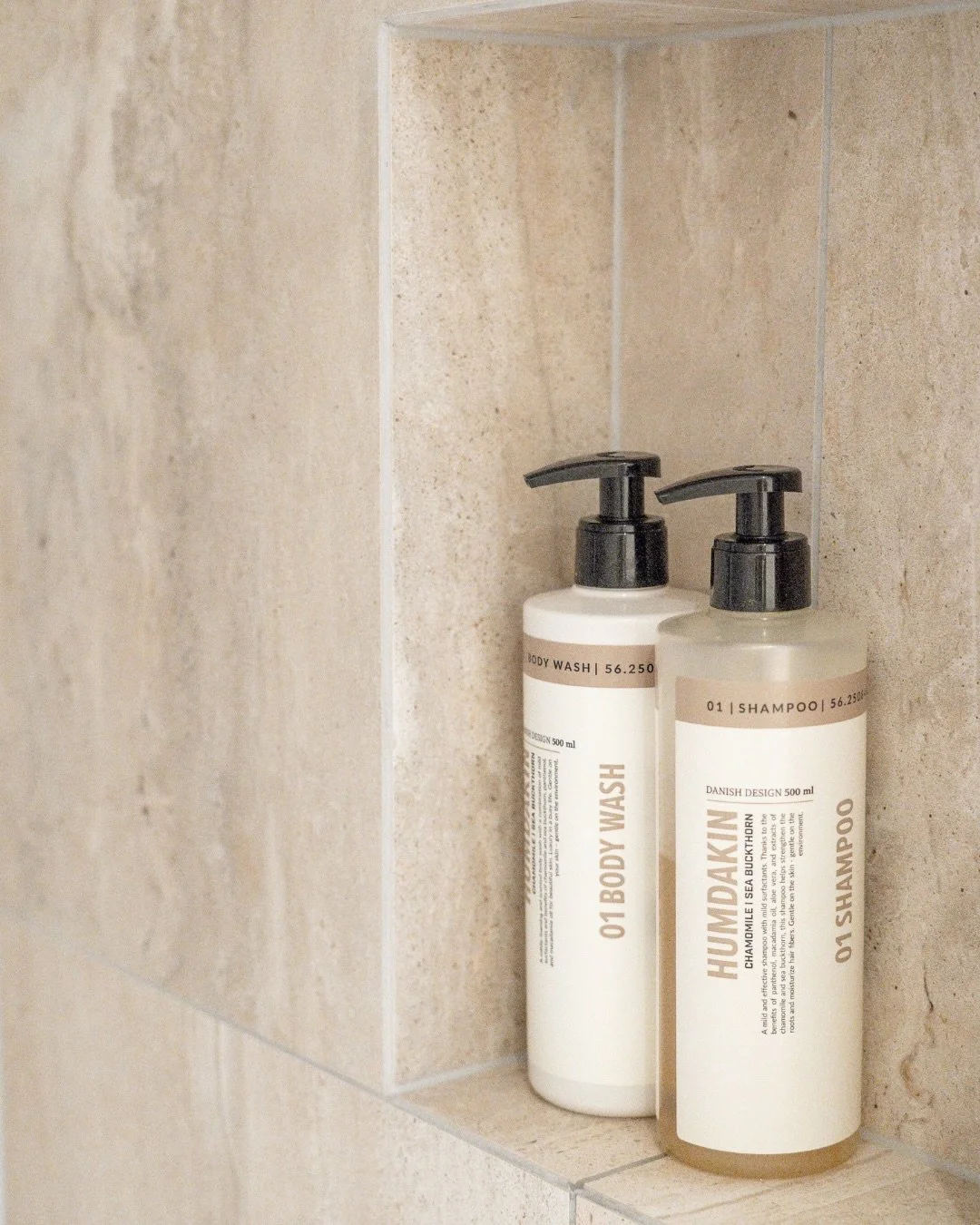 To beige shampoo- og balsamflasker med sorte pumpdispenser i en badeværelseskarm