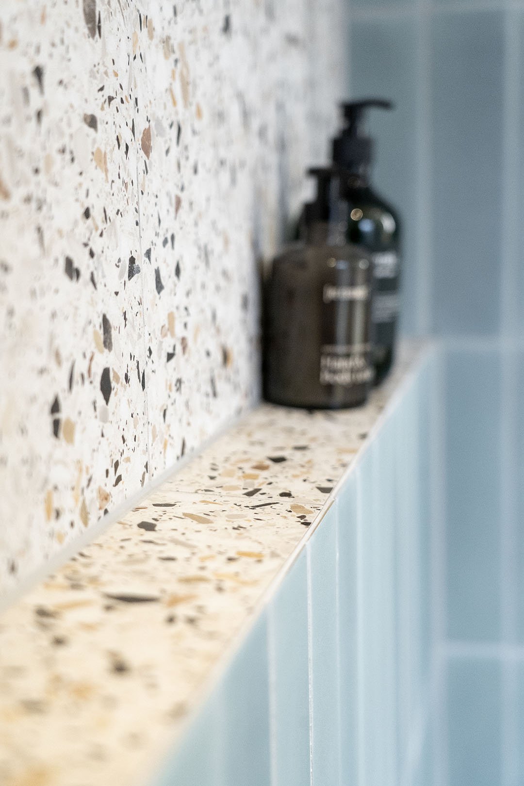 Fliser med terrazzo-mønster og badeværelsestilbehør, herunder en sort flydende sæbe dispensers