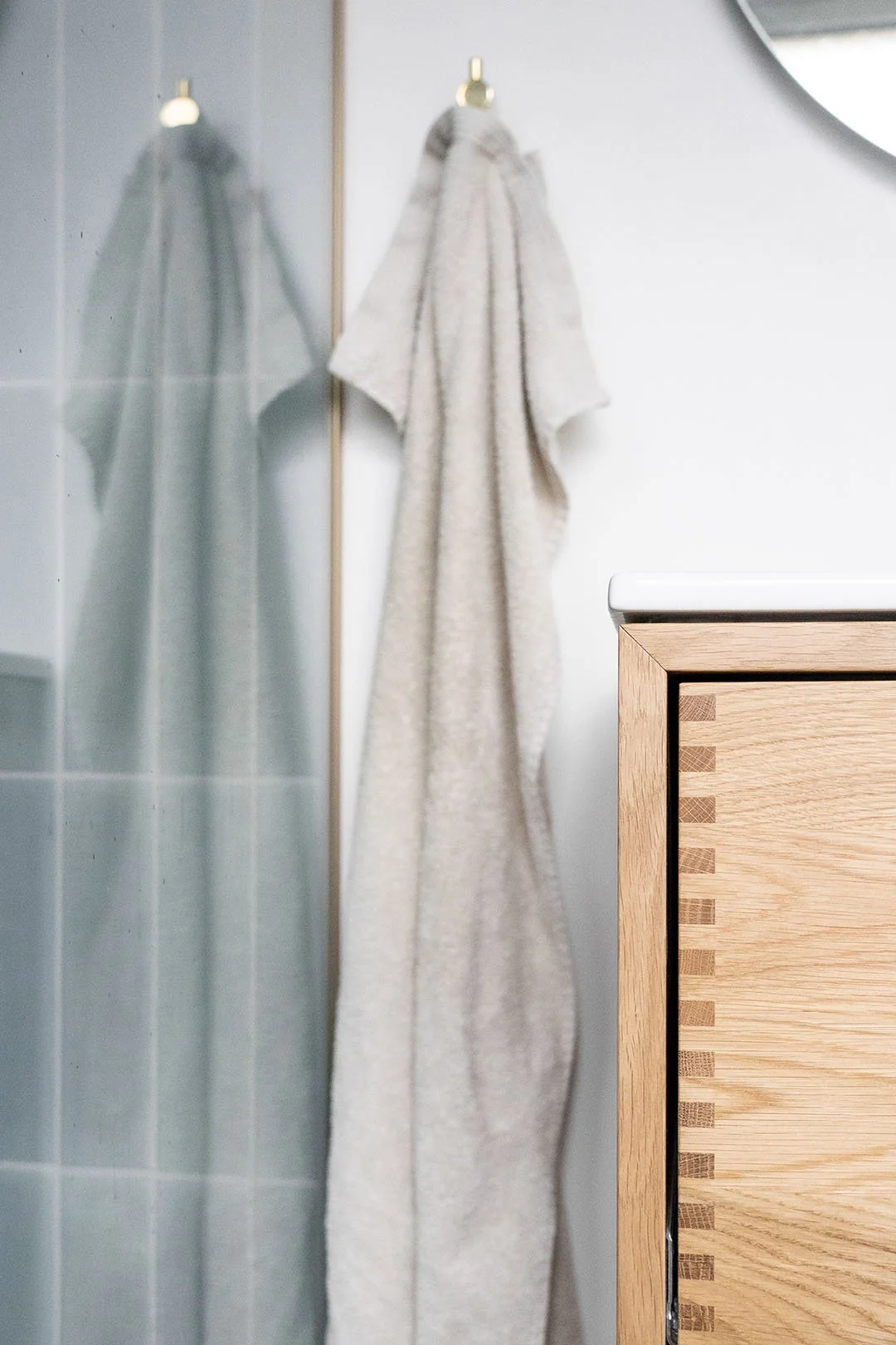 En badekåbe hænger på en messing håndkædekrog i et badeværelse ved et egetræsmøbel.