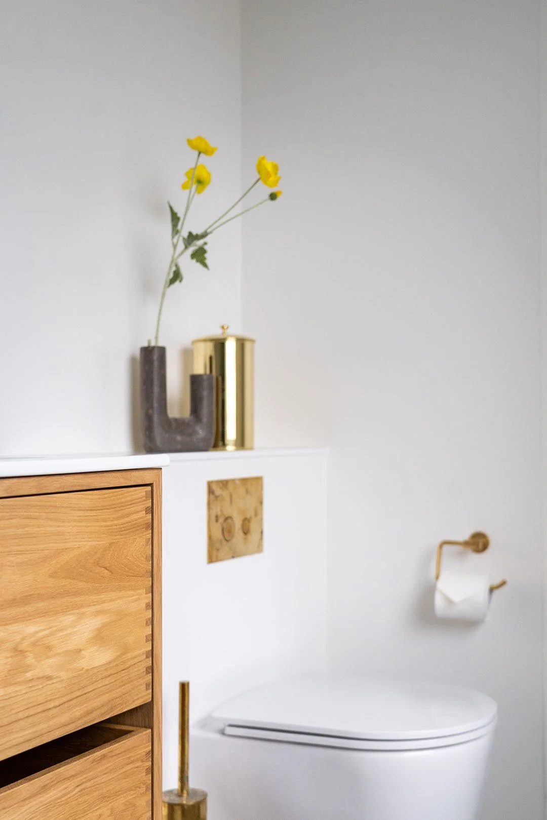 Moderne badeværelse med toilet, træskab, guldkande og guldbestik på væggen, hvid væg og dekoration.