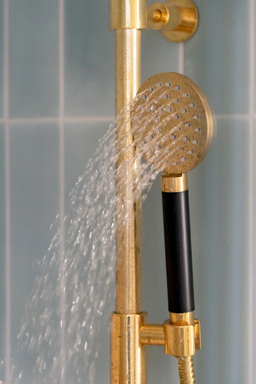 Messing håndbruser i brusebad med blå fliser.