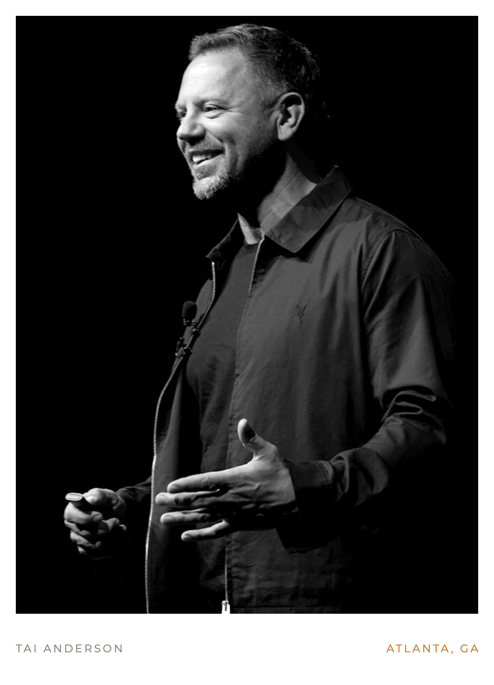 Black and white photo of Tai Anderson speaking on stage, smiling and gesturing with his hands, in Atlanta, Georgia.
