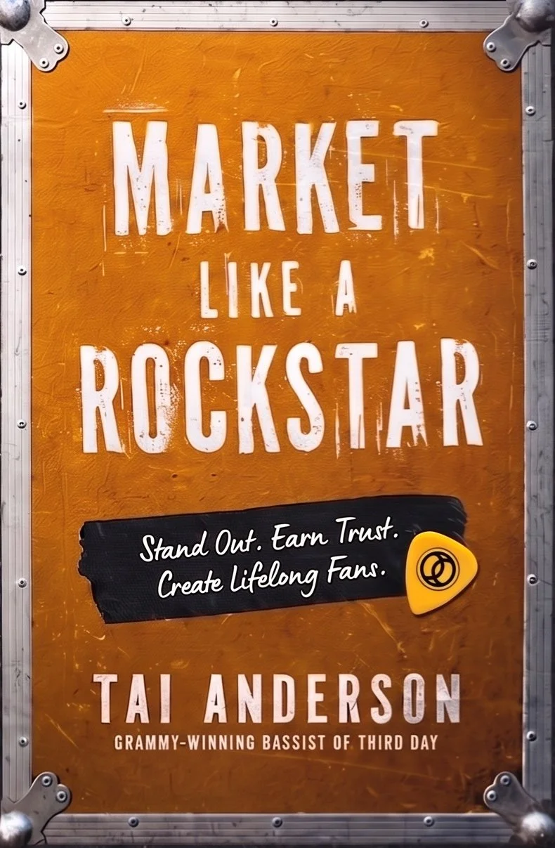 A sign with an orange background and white text that reads "Market Like a Rockstar". Below, there is a black section with white cursive writing saying "Stand Out. Earn Trust. Create Lifelong Fans." and a small yellow guitar pick icon. The name "Tai Anderson" appears at the bottom with the note "Grammy-winning Bassist of Third Day".