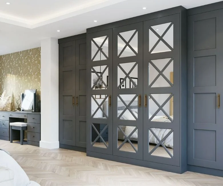 Modern bedroom with dark gray built-in cabinets and glass sliding doors with geometric cross patterns, light-colored wood flooring, and a vanity table with a mirror.
