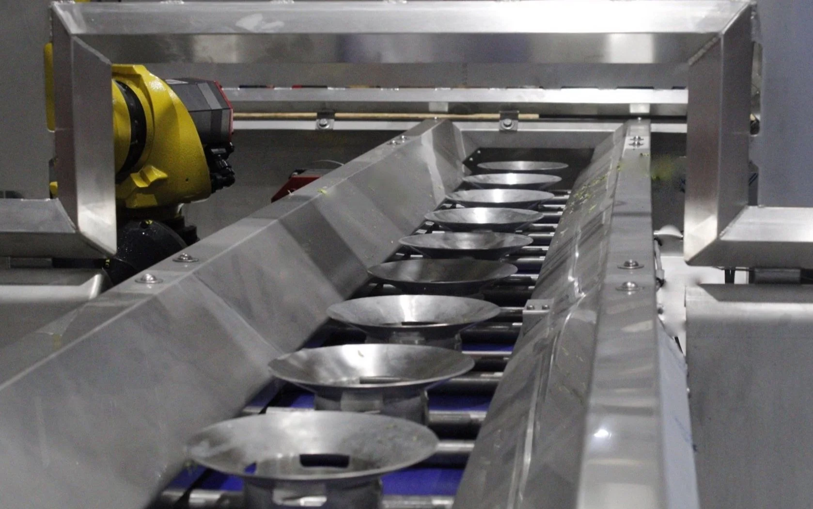 Close-up of an Extractacore® conveyor system with metal bowls and a robotic arm.