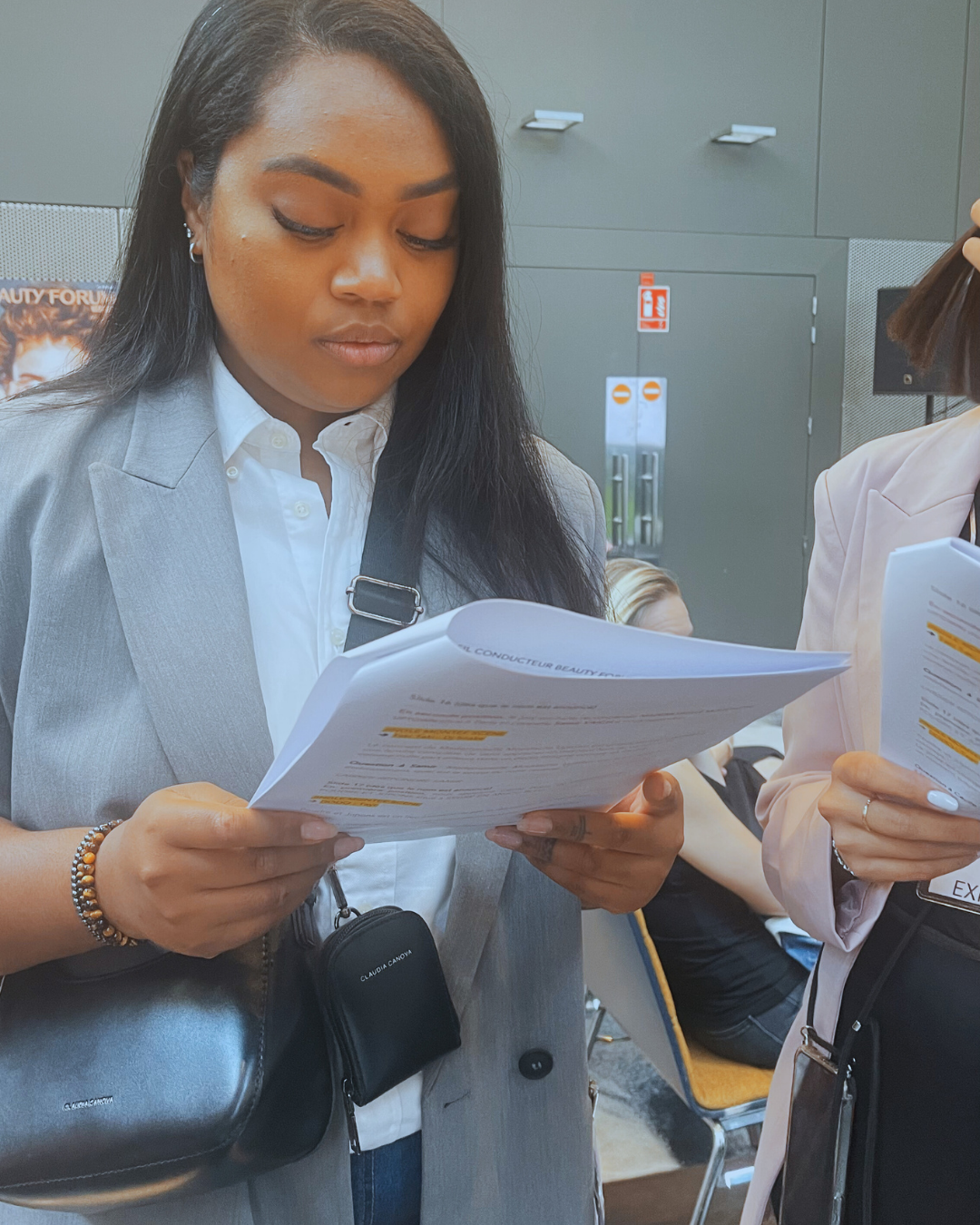Une femme d'affaires avec un blazer gris et une chemise blanche lit attentivement un document dans un environnement professionnel.