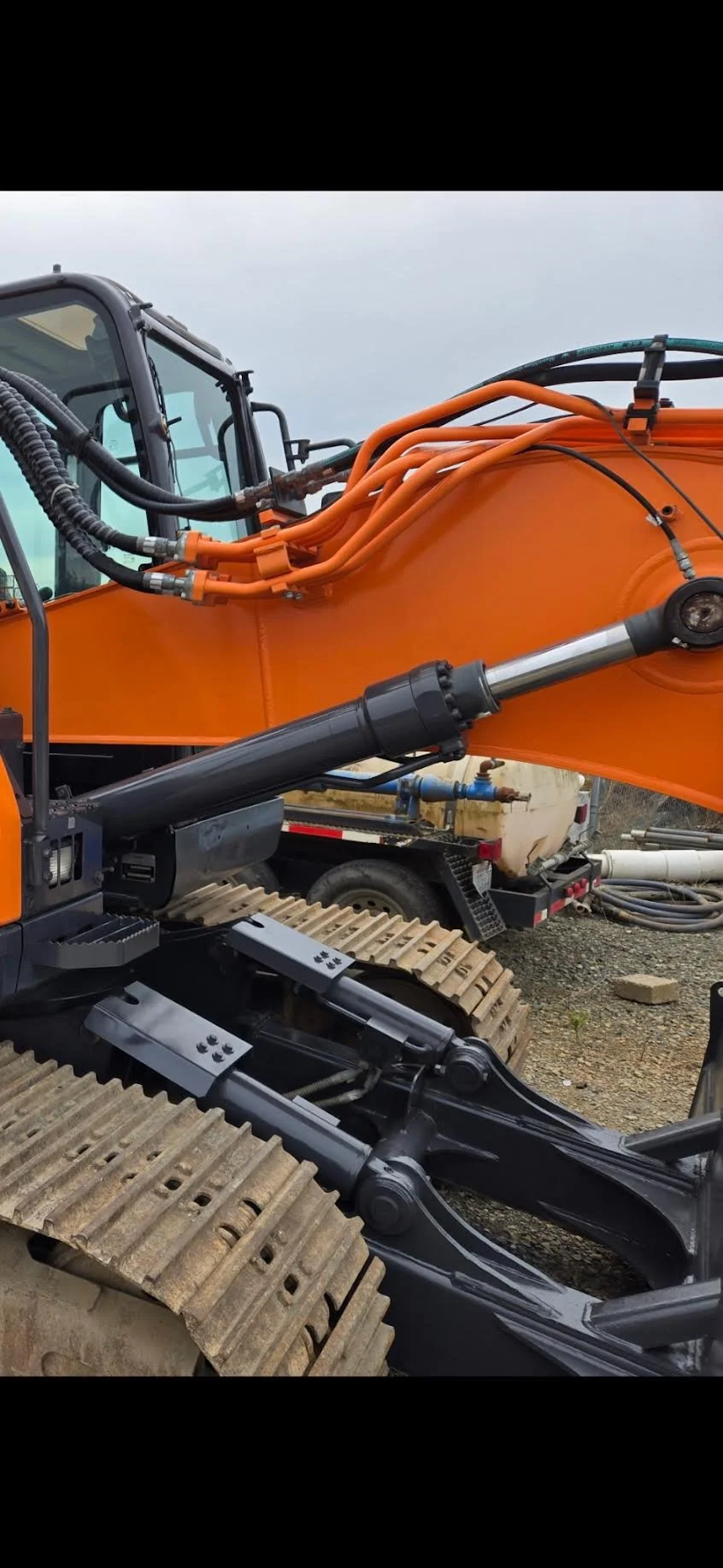Close-up of an orange and black excavator with hydraulic pipes and a tracked wheel.