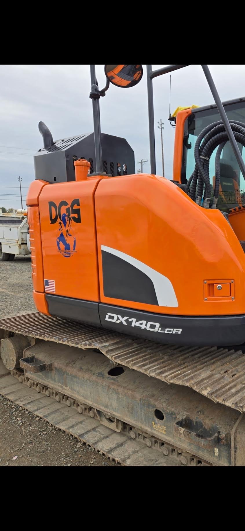 Close-up of an orange excavator with the model number DX140LCR, resting on a dirt construction site.