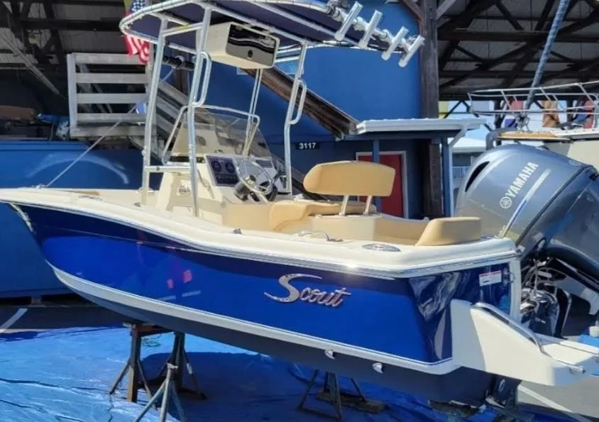 A blue and white Scout motorboat with beige seats, mounted on stands at a boat show, with a Yamaha outboard engine.