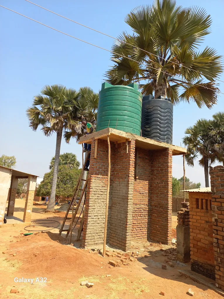 Water tanks on a brick and wooden shelter platform, with palm trees in the background, in a rural area.