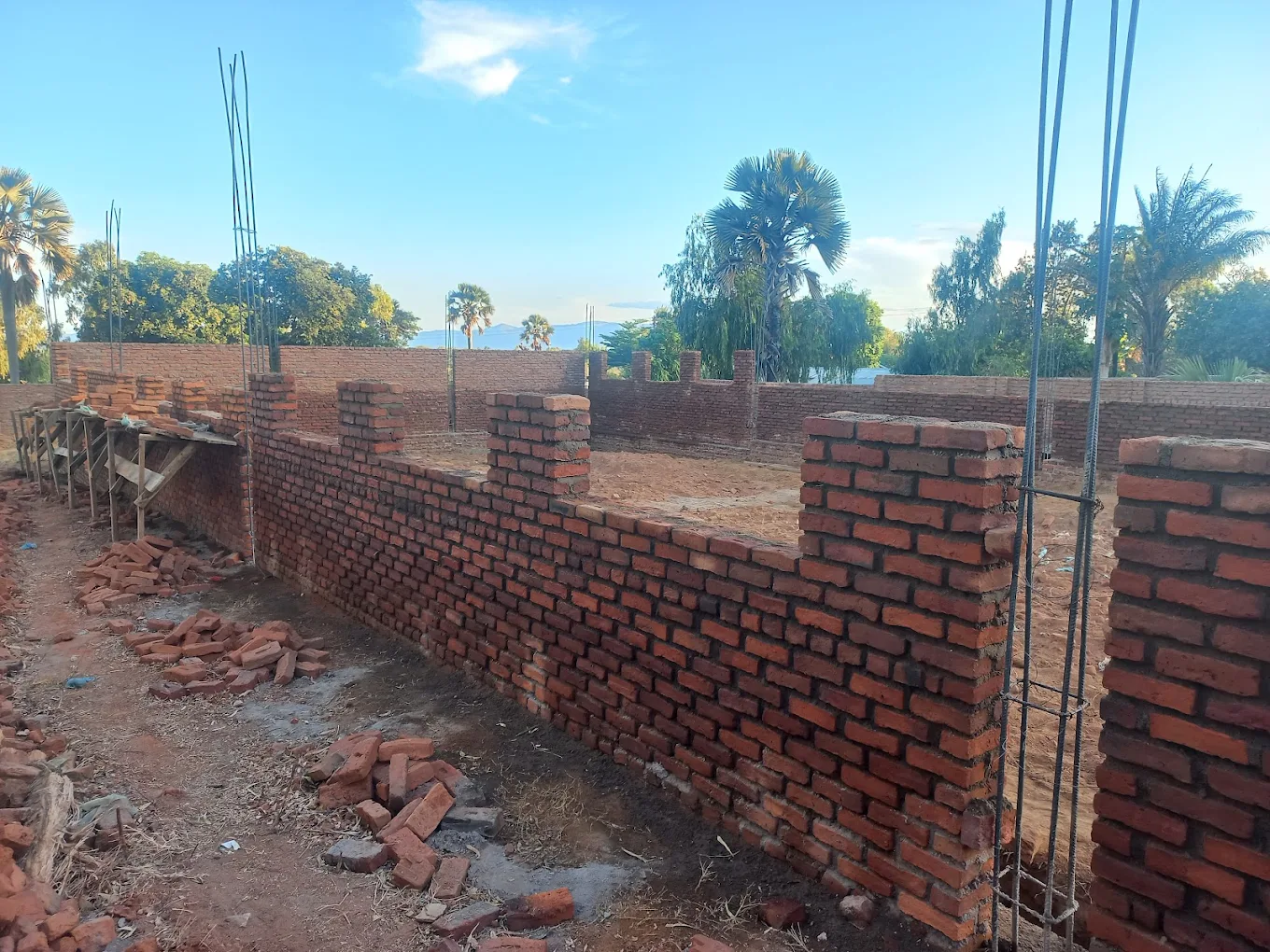 Construction site with a partially built brick wall and trees in the background under a clear sky. New Palm Africa Huckleberry Fox Foundation