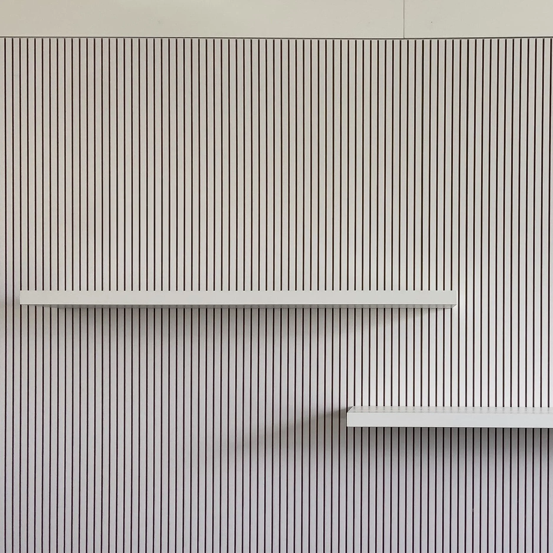 Zwei weiße Wandregale vor einer Wand mit vertikalen schwarzen Linien.