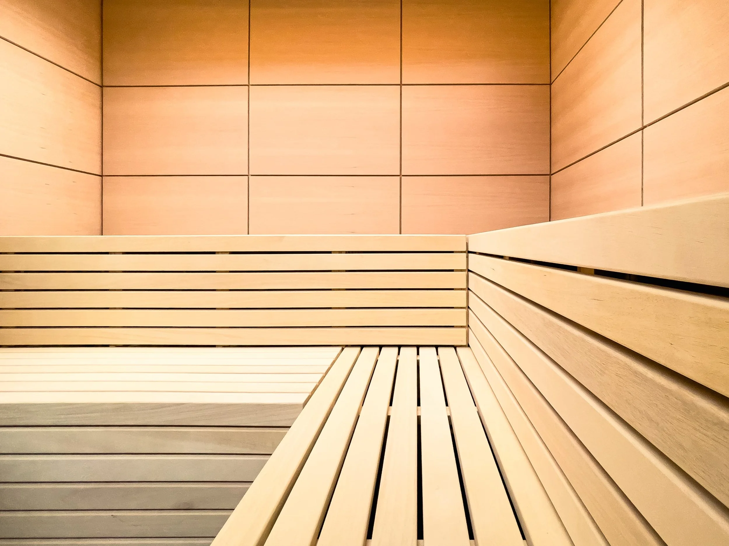Innenansicht einer Sauna mit hölzernen Bänken und goldbraunen Wandfliesen