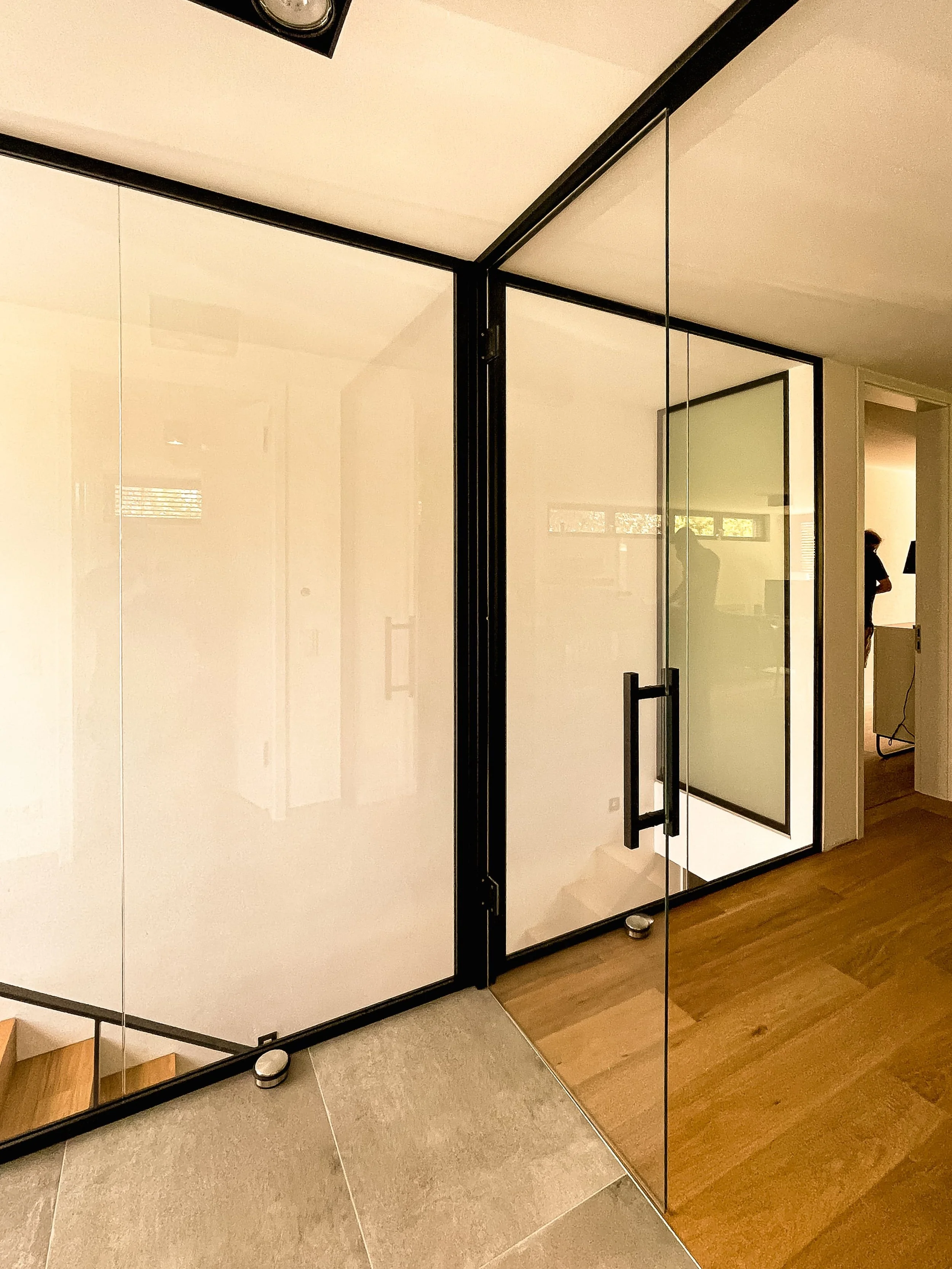 Moderner Raum mit Glastüren, Holz- und Fliesenboden, mit sichtbarer Treppe und Person im Hintergrund