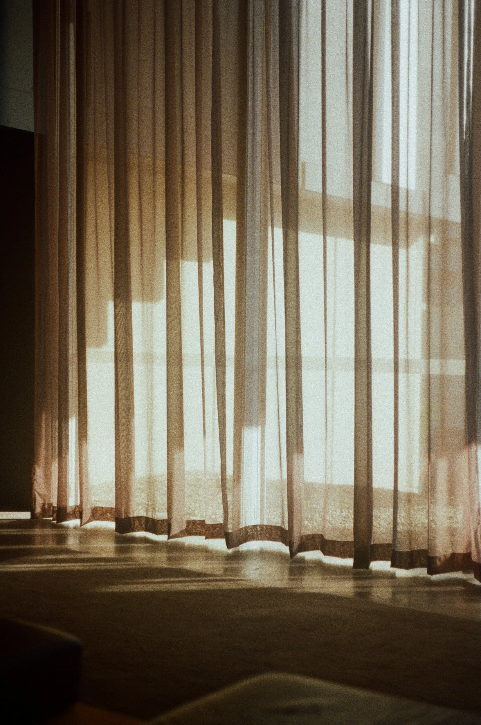 Sheer curtains with sunlight streaming through onto a floor.