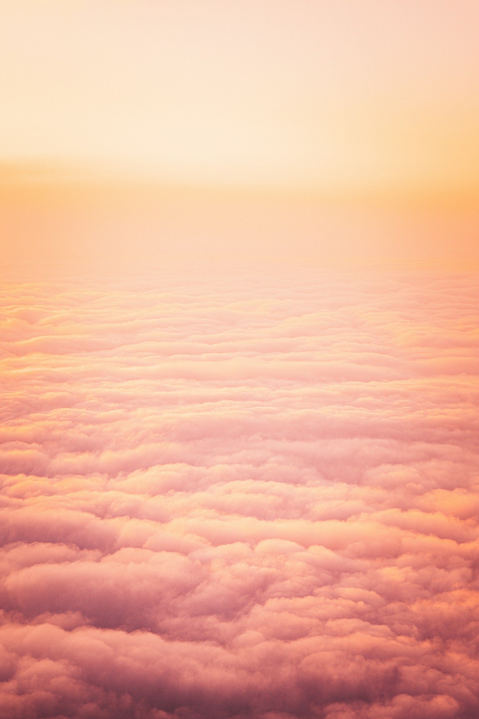 A view of pink and orange clouds from above, with the sky glowing in soft pastel colors during sunrise or sunset.