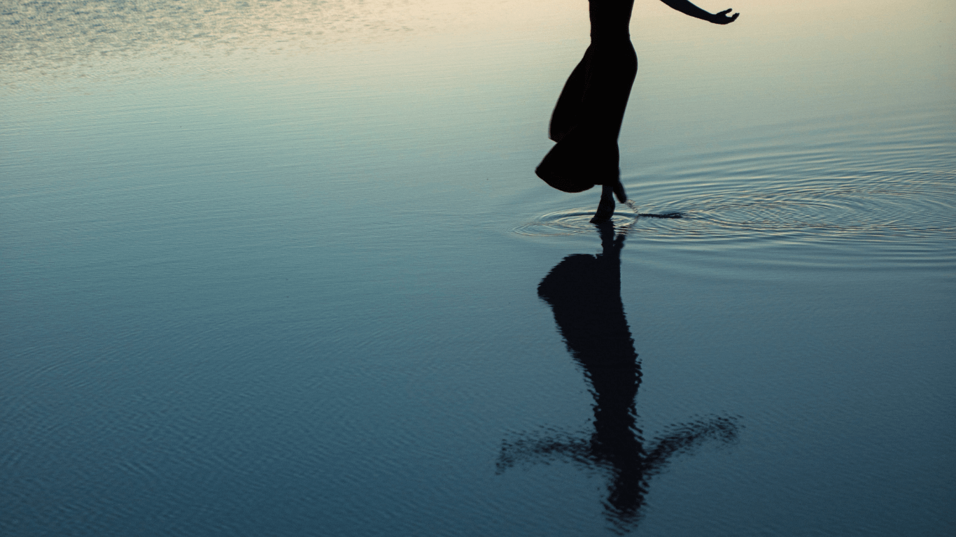 Silhouette of a woman standing calmly in water, reflected beneath her, representing internal power and self-trust.