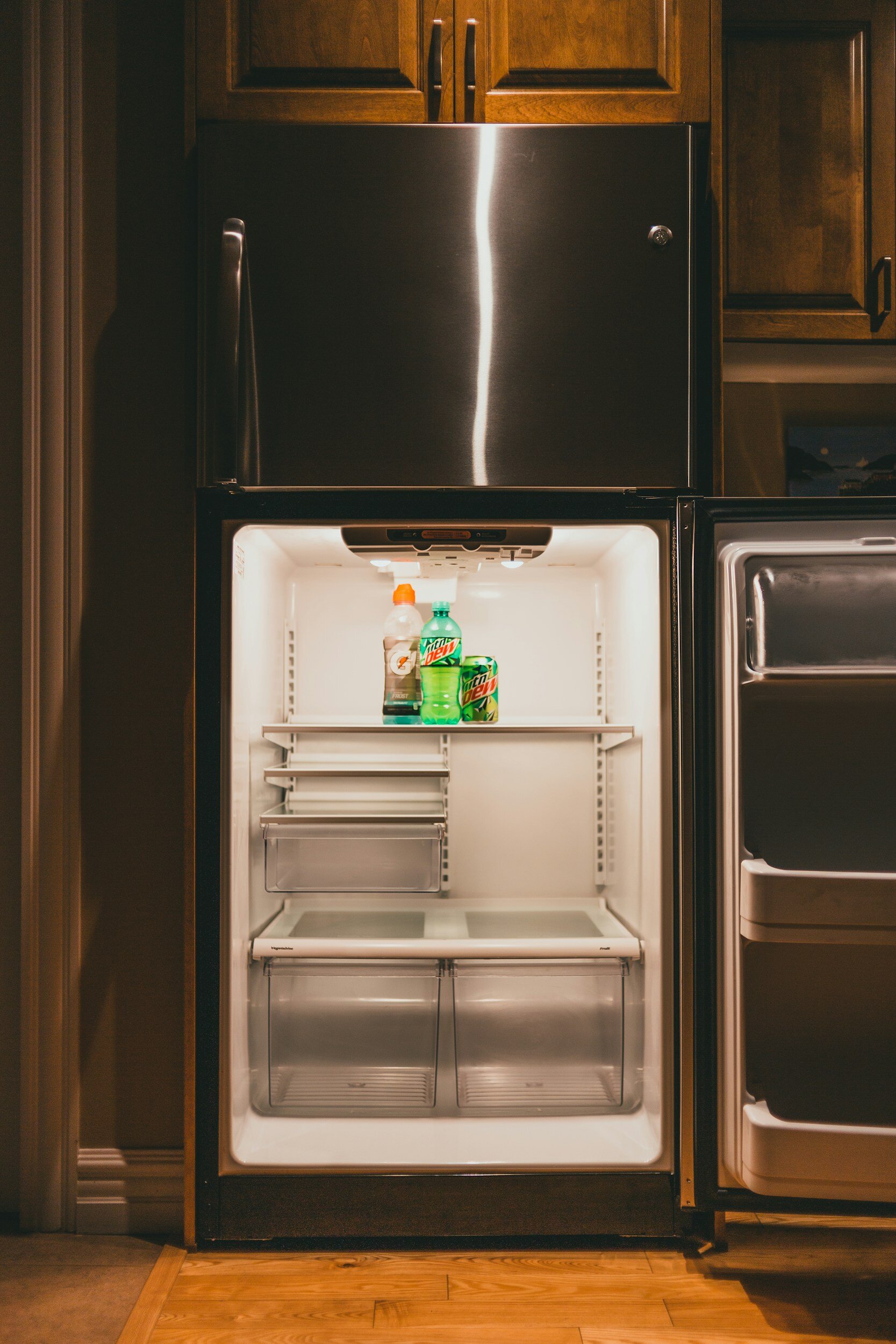 Empty refrigerator with a few bottles of Mountain Dew and other beverages on the top shelf.