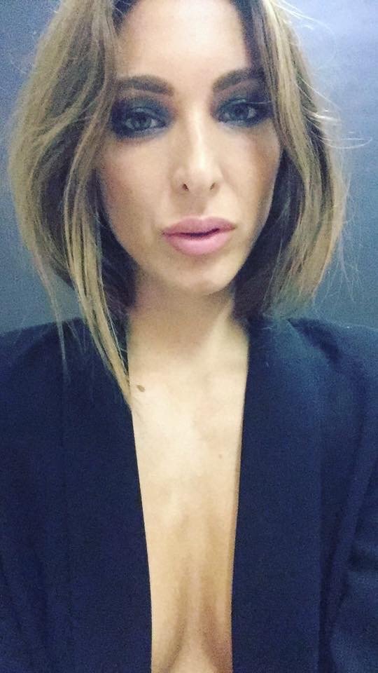 Dostinja with smokey eye makeup and pink lipstick, wearing a black top, with shoulder-length hairstyle.