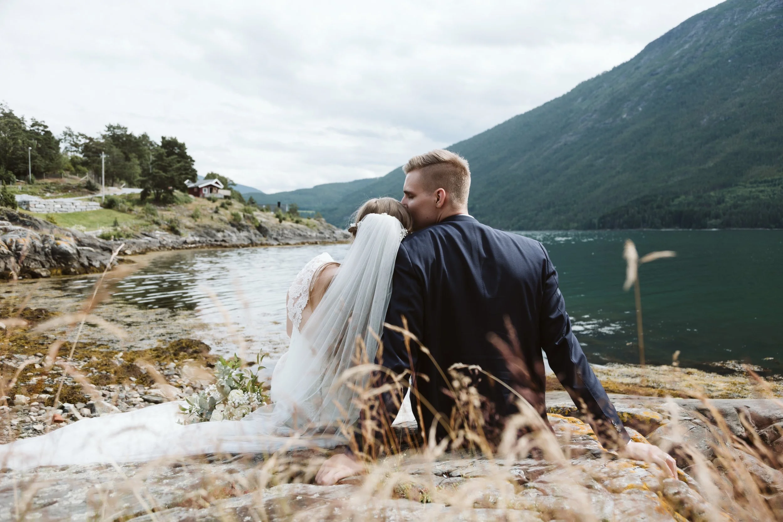 Et ektepar, enn sitte på en stein ved vannet omgitt av fjell i Norge.