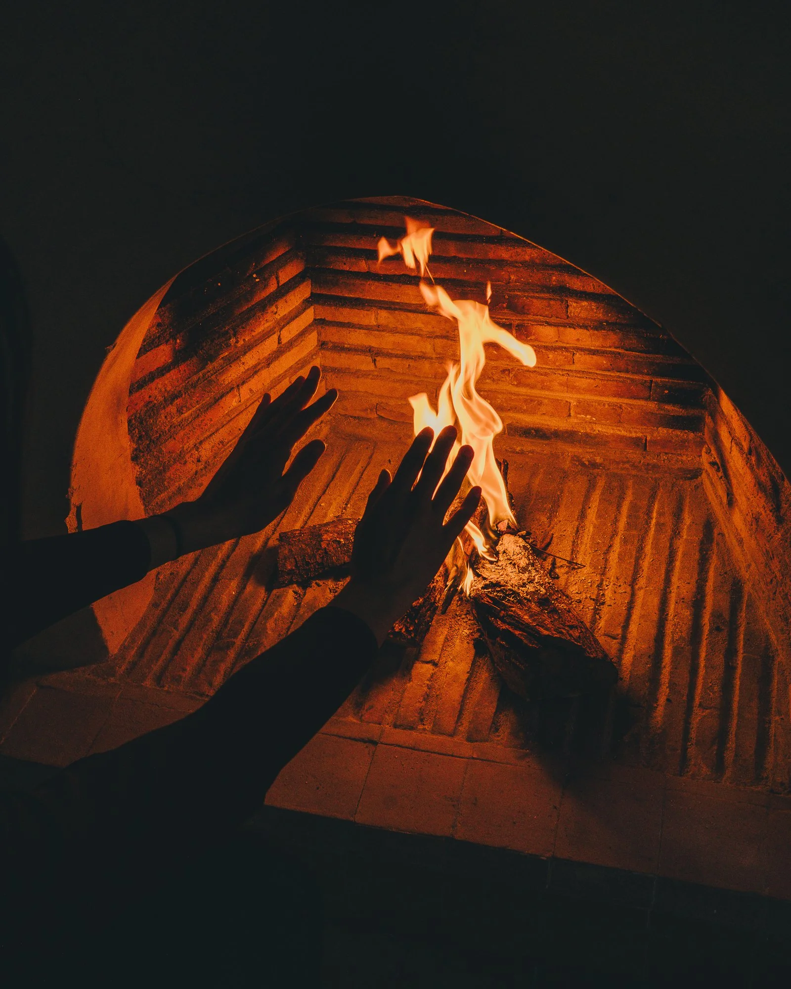 Person tending a small fire in a brick fireplace with their hands.