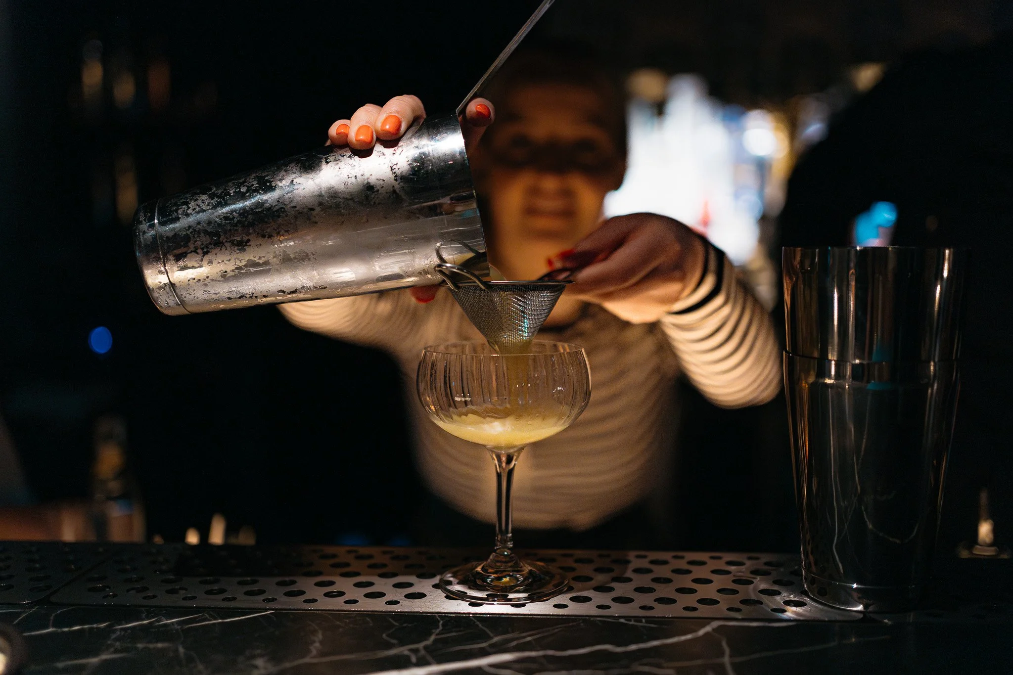 Barkeeper gießt einen Cocktail durch ein Sieb in ein Cocktailglas auf einer Bar
