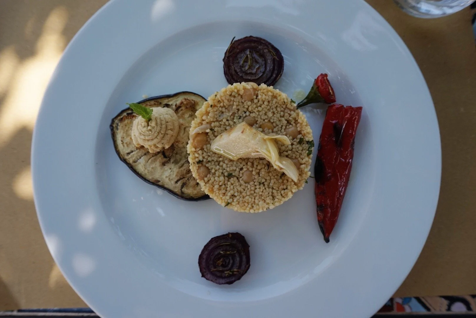 Plate with couscous, roasted eggplant, red pepper, red onion, and artichoke garnish