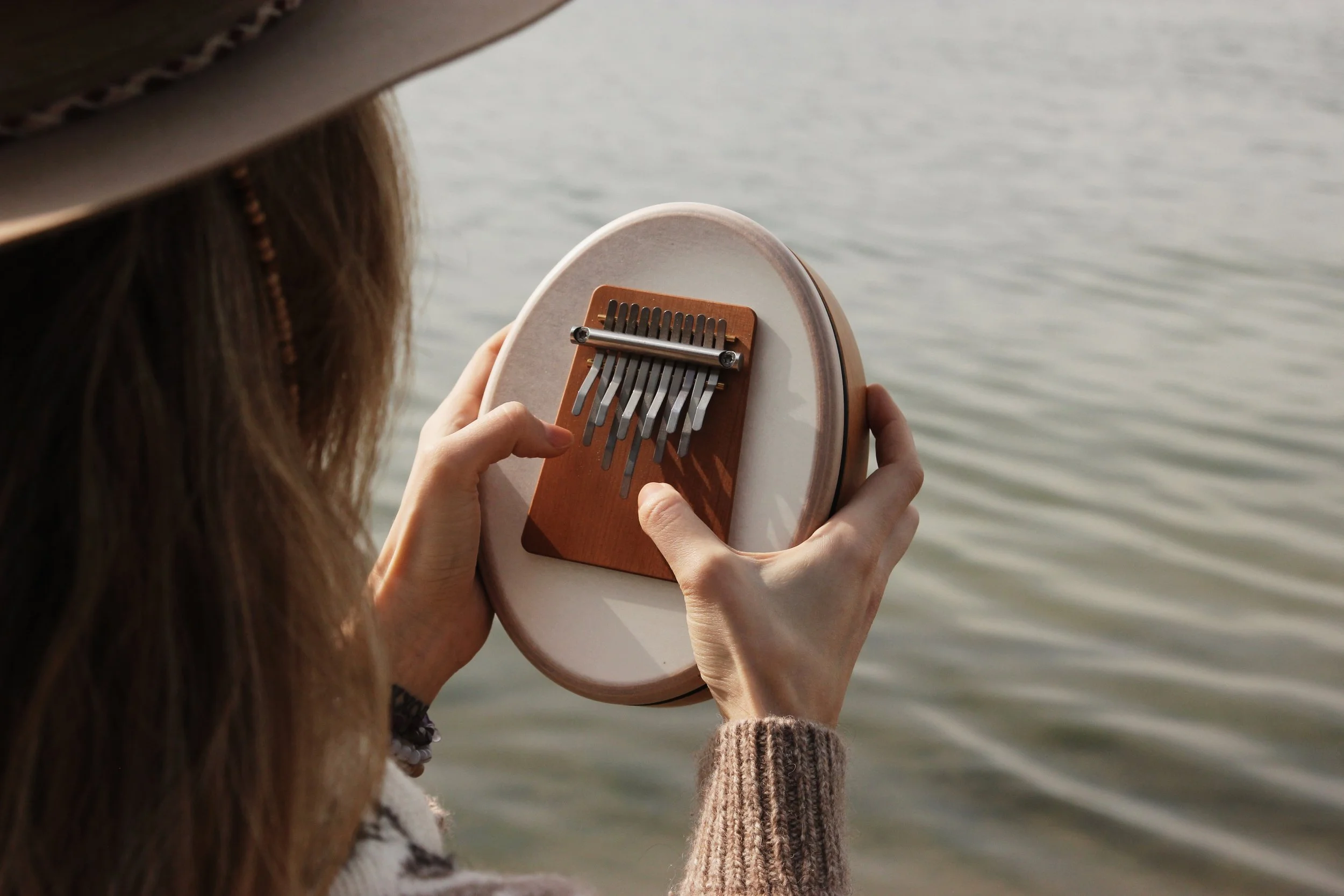 Person playing a kalimba by a body of water