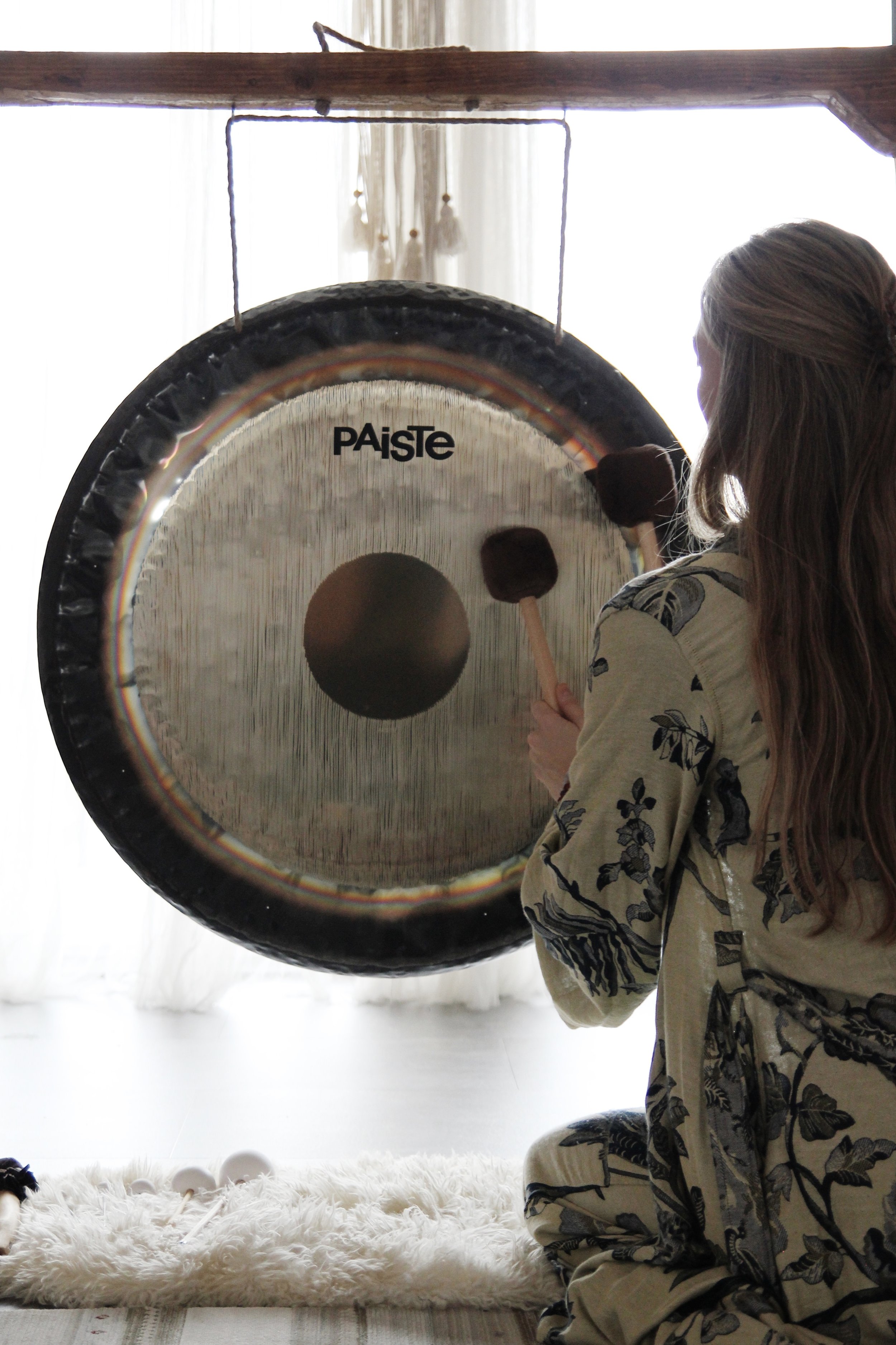 Person playing a large Paiste gong with mallets, sitting on a carpet.