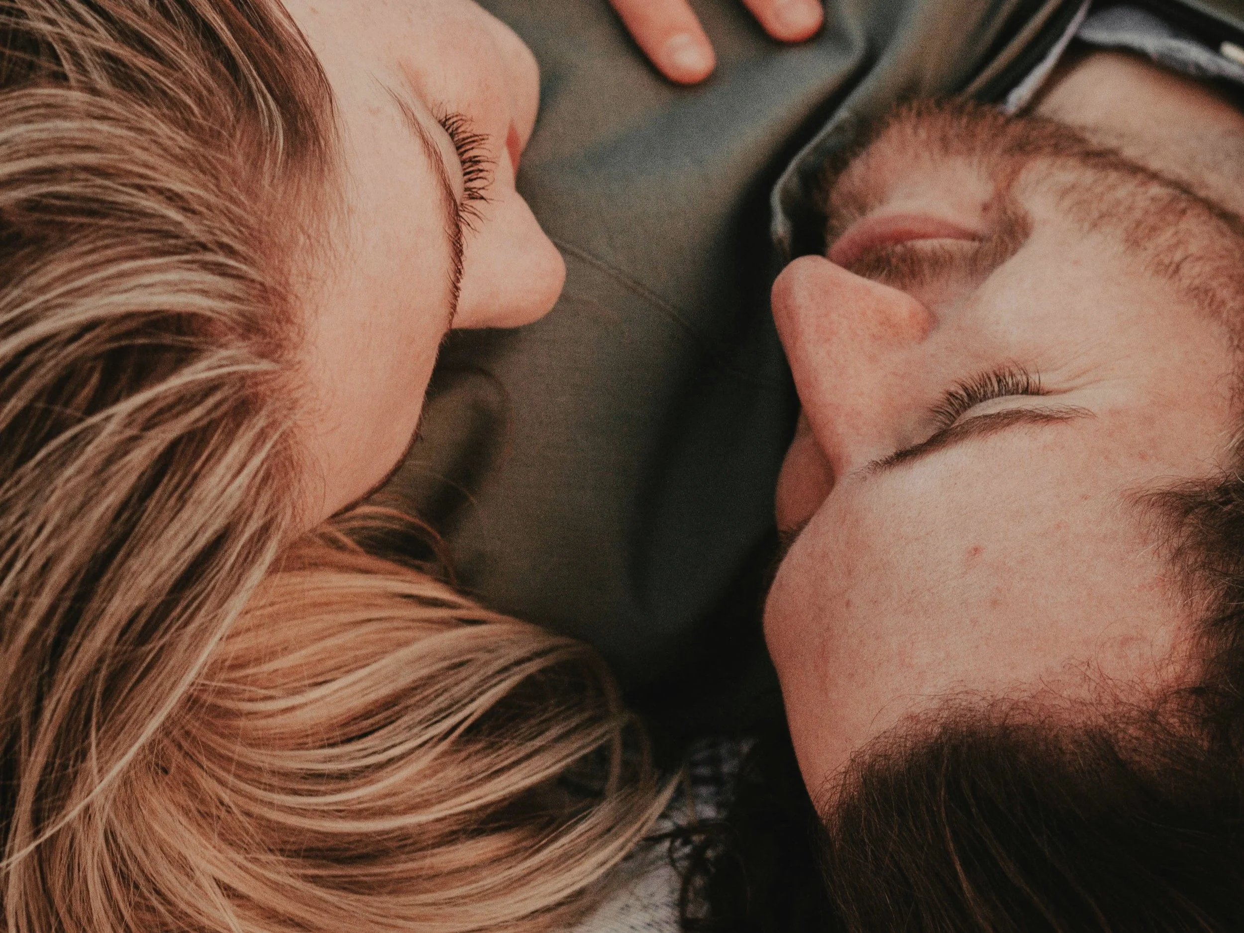 Close-up of two people lying head-to-head, eyes closed, with soft lighting.