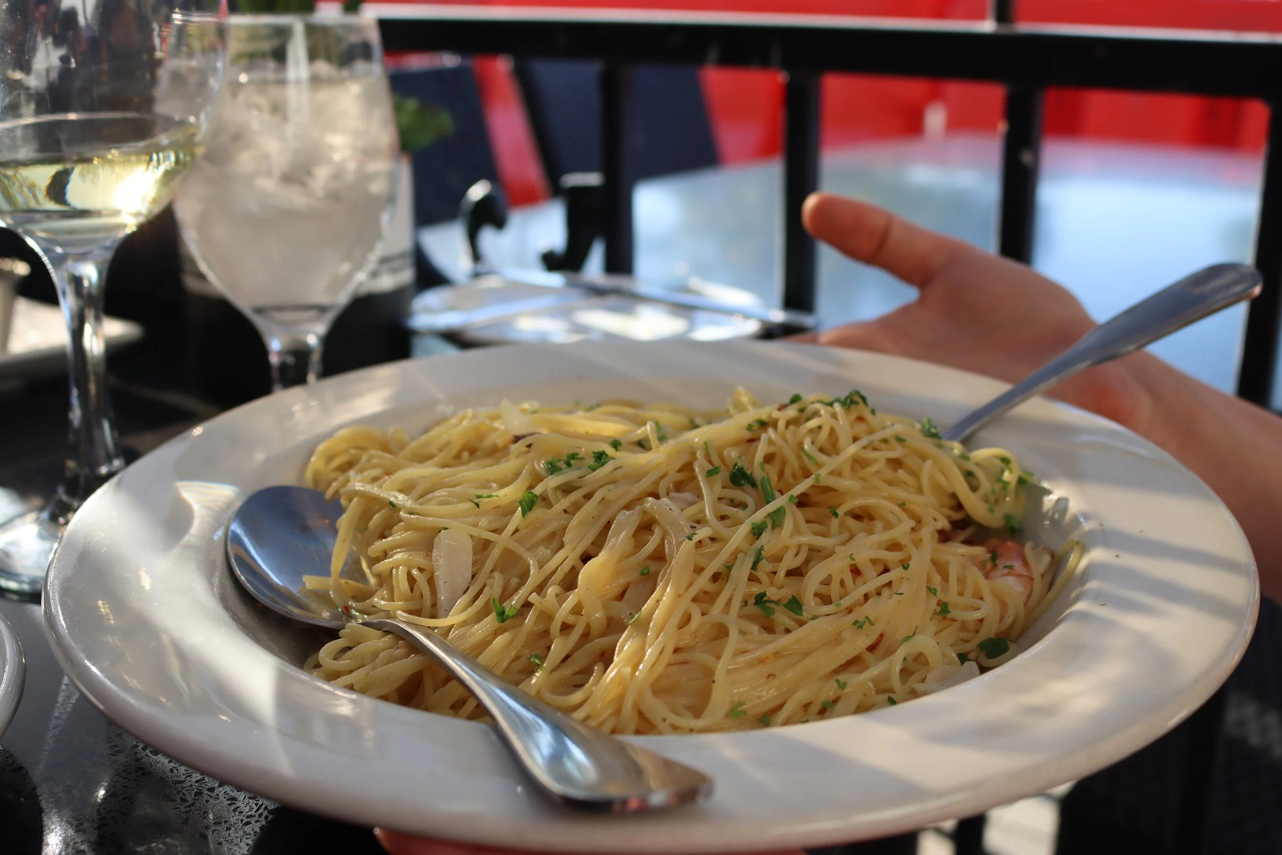 A plate of spaghetti with herbs on a table, with glasses of white wine and water in the background.