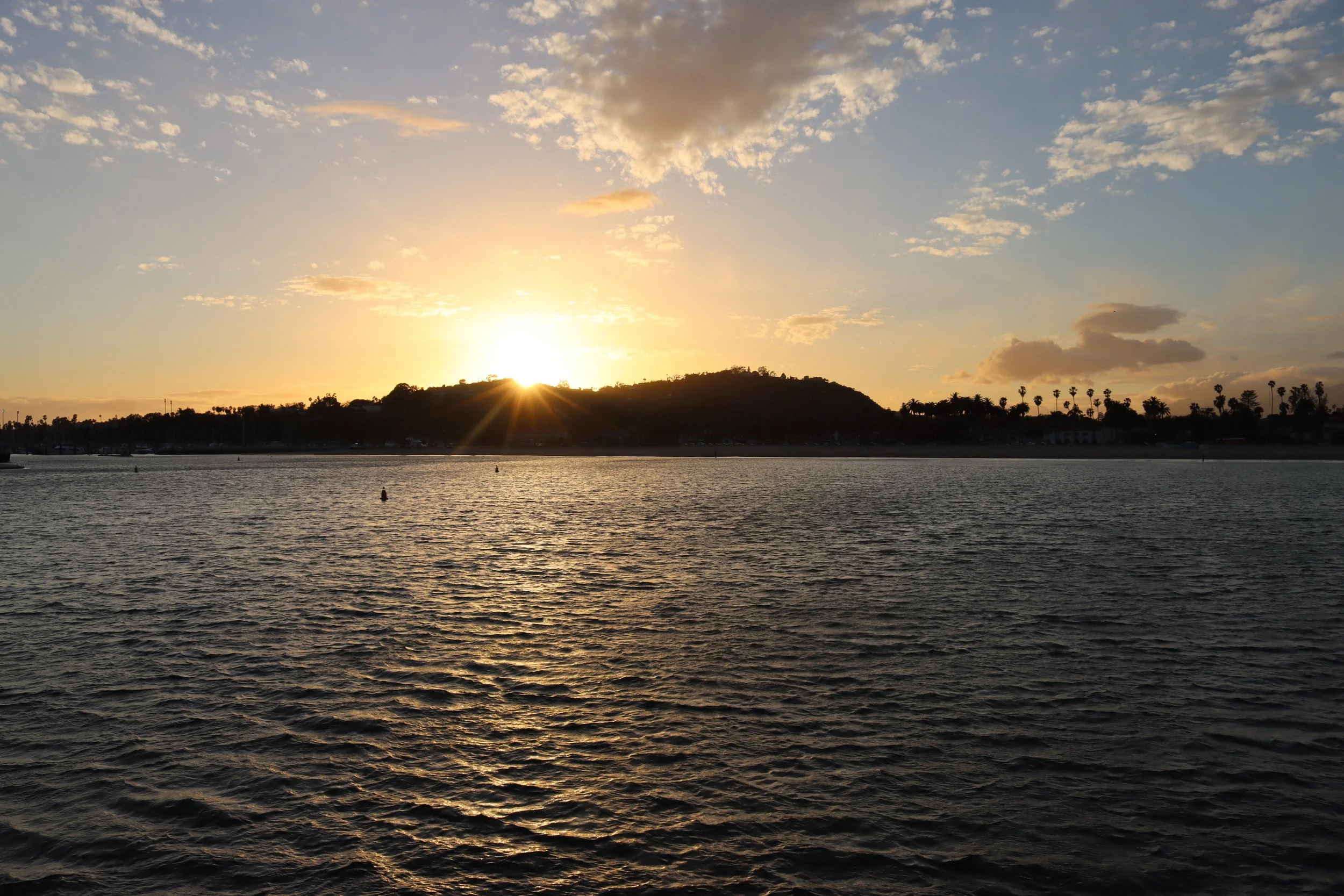 Sunset over a body of water with a hill and trees in the distance.
