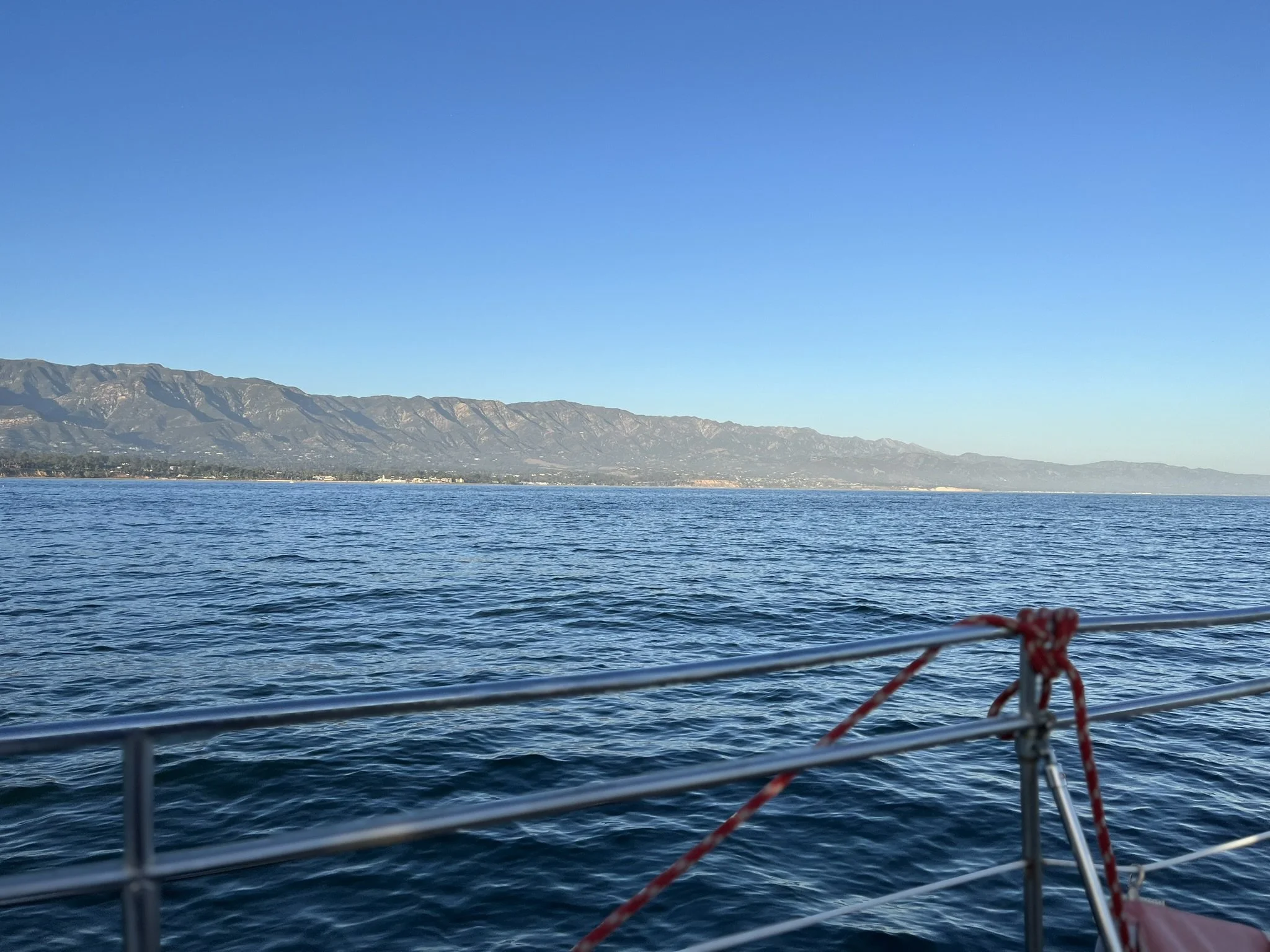 View of ocean with mountain range in the background, taken from a boat with metal railing in the foreground.