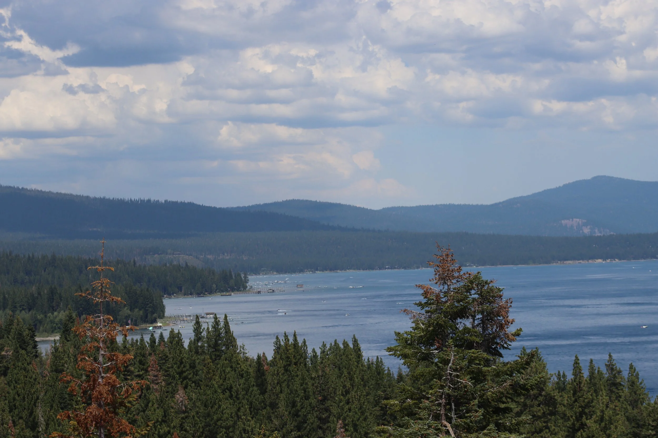 Scenic view of a forested lake with mountains in the background under a partly cloudy sky.