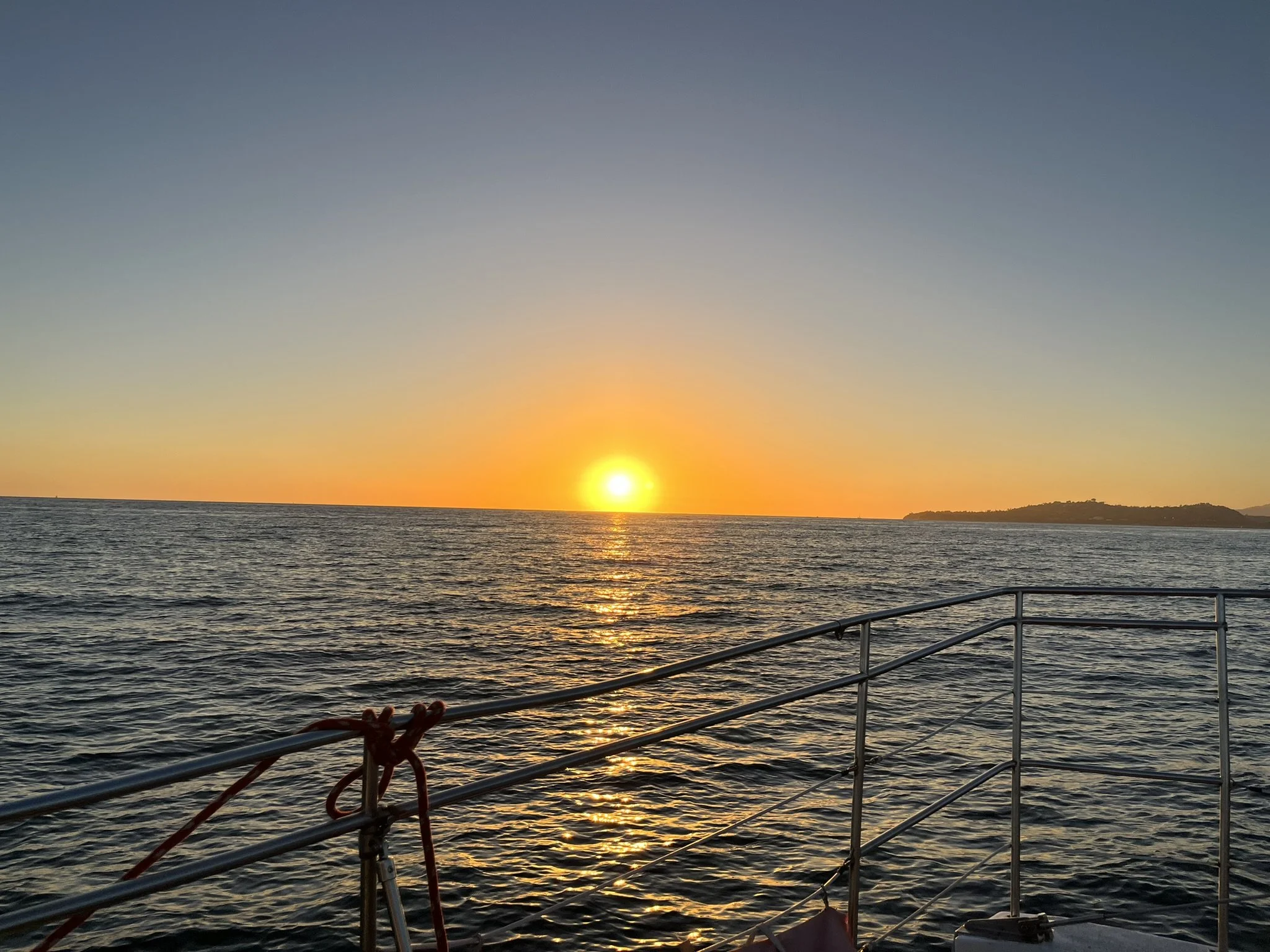 Sunset over the ocean viewed from a boat with railings and red ropes