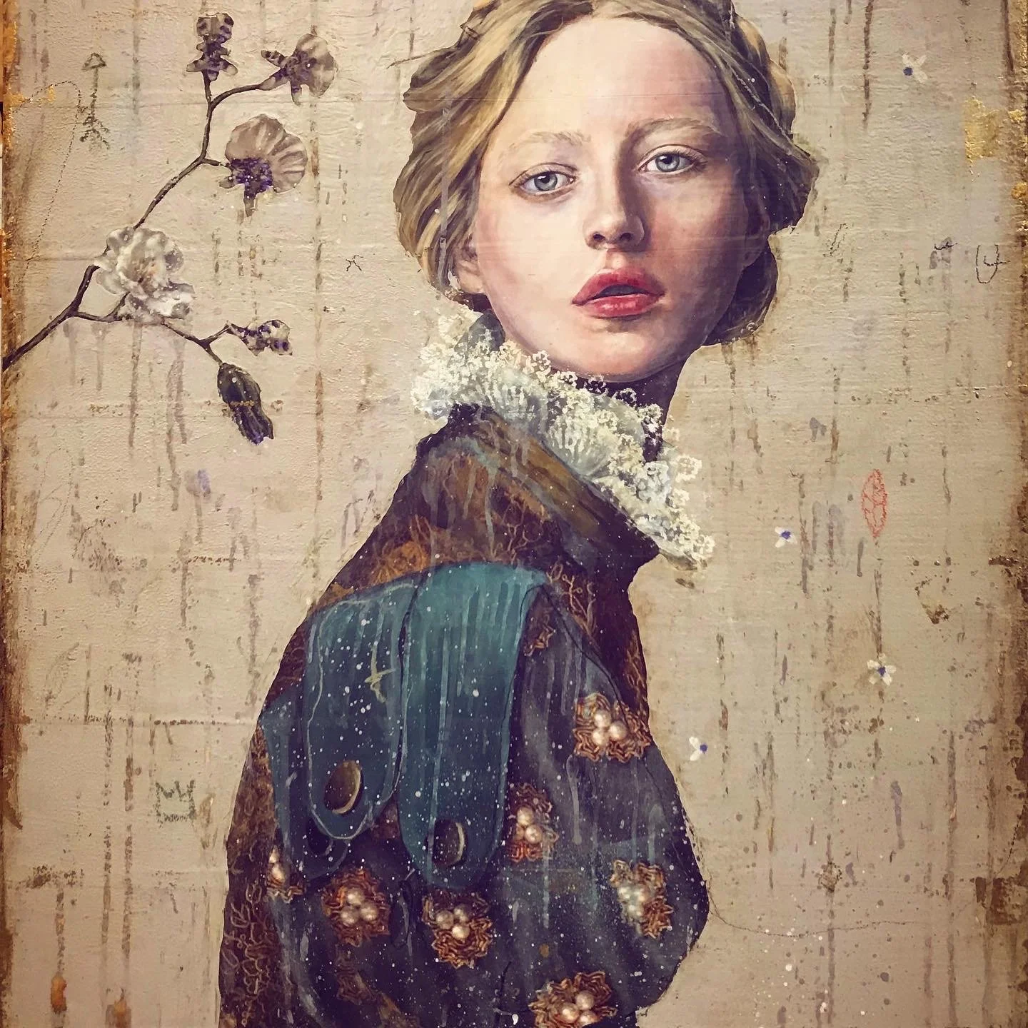 A portrait of a woman with blonde hair and blue eyes, wearing a patterned garment with floral design and a lace collar. There is a branch with flowers to her left, and the background features textured, weathered surface.