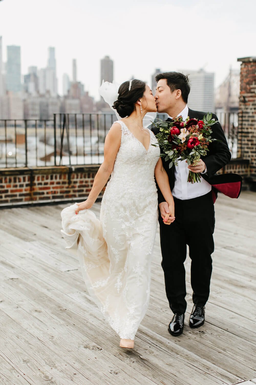 Bride and groom share a kiss on a city rooftop, with the New York skyline in the backdrop, epitomizing urban elegance.
