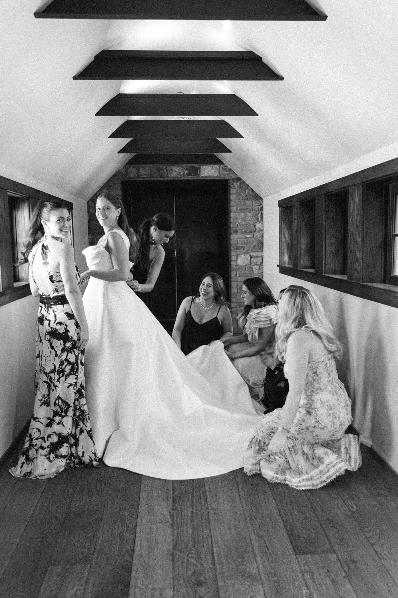 Bride in a stunning white dress surrounded by bridesmaids in an attic space, preparing for the ceremony.