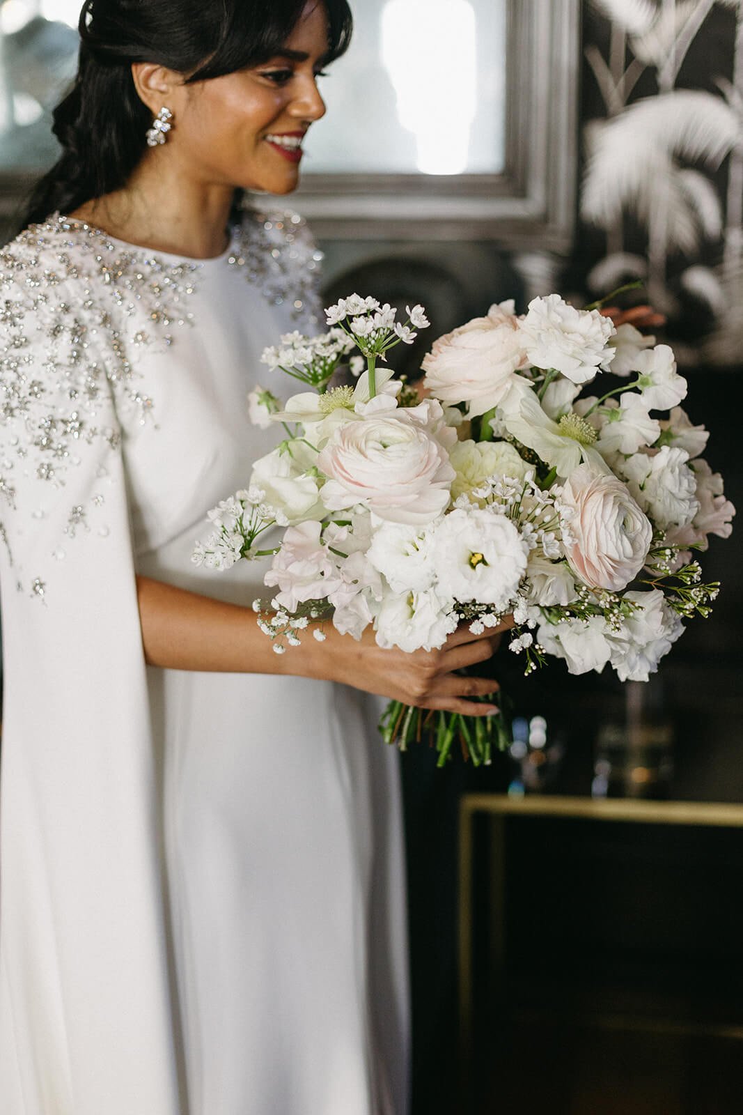 Bride in a beautifully detailed gown holding a lush bouquet, ready to walk down the aisle.