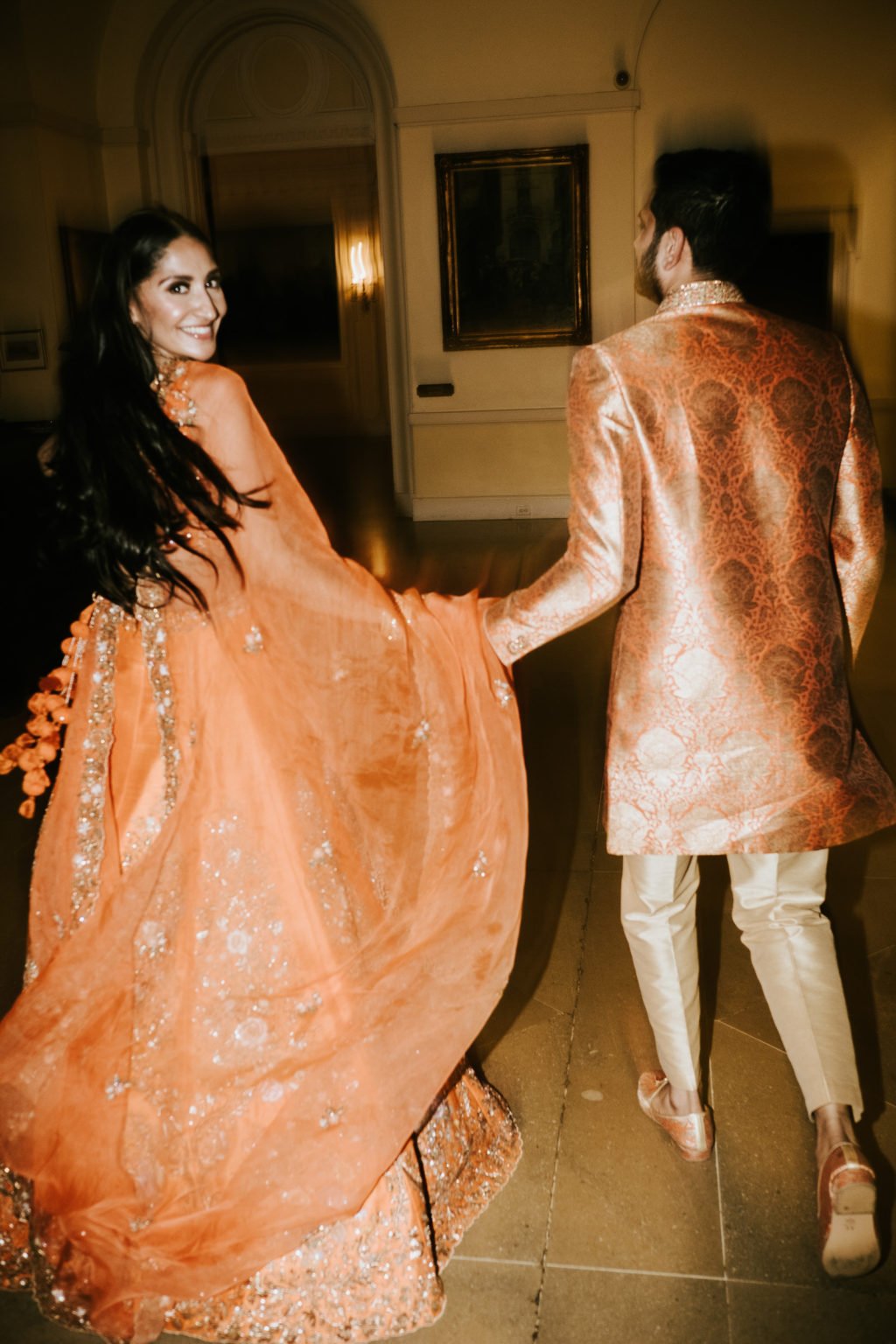 Bride in an orange and gold Saree, with the groom in an orange Achkan