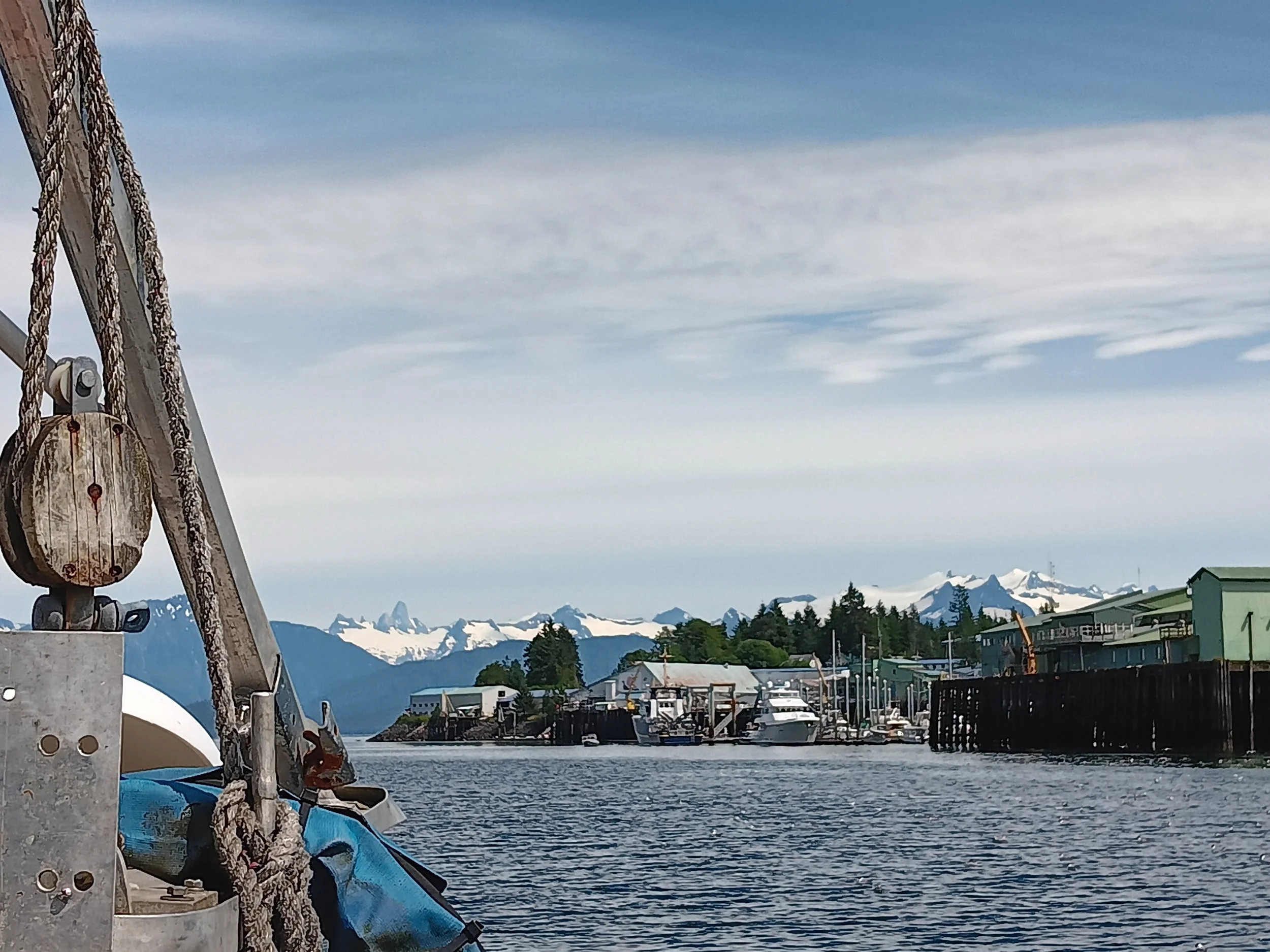 A scenic view of a harbor with boats and docks, snow-capped mountains in the background, and a partly cloudy sky.