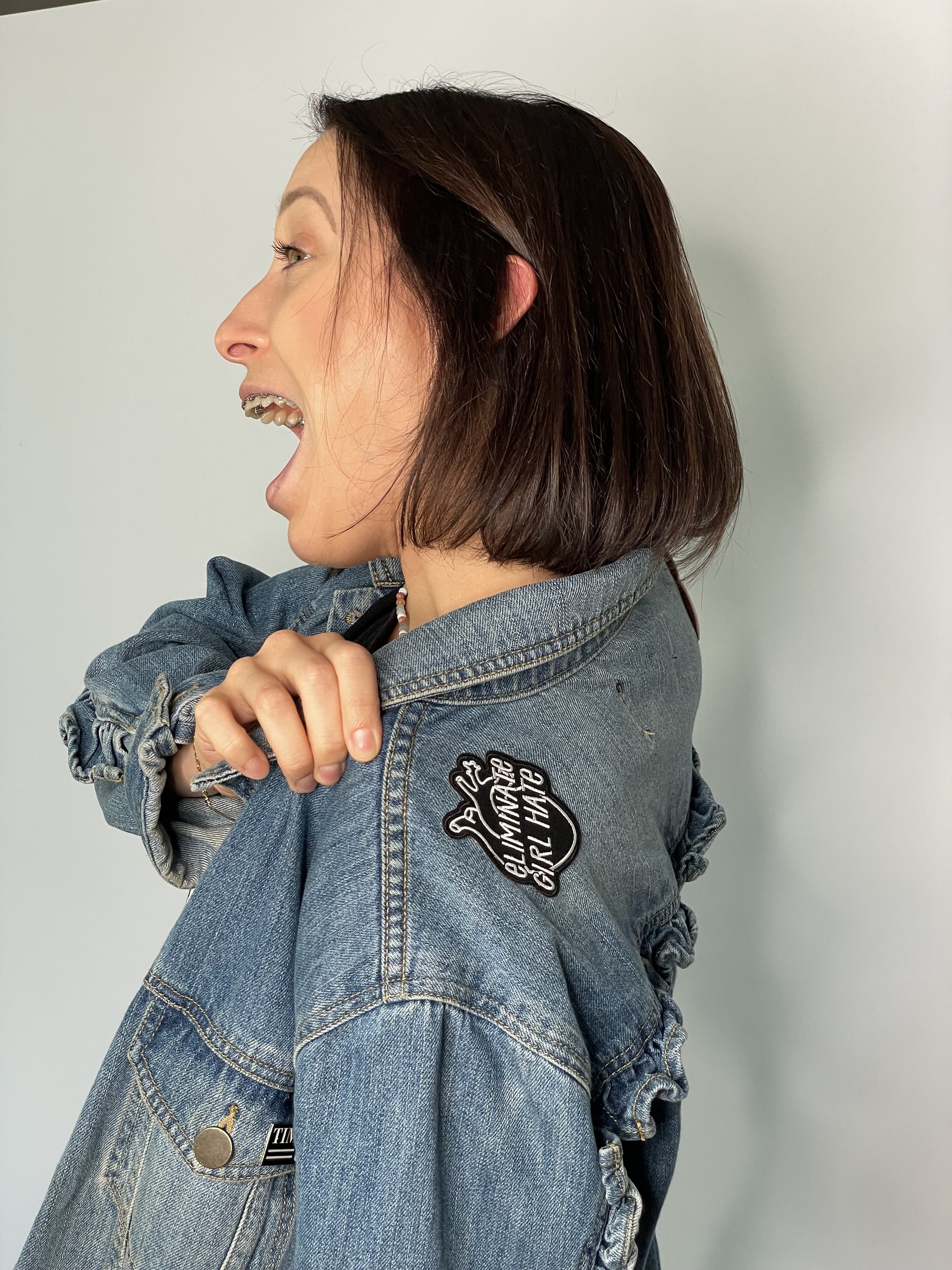 Young woman wearing the black and white embroidered ELIMINATE GIRL HATE embroidered Iron-On Patch product