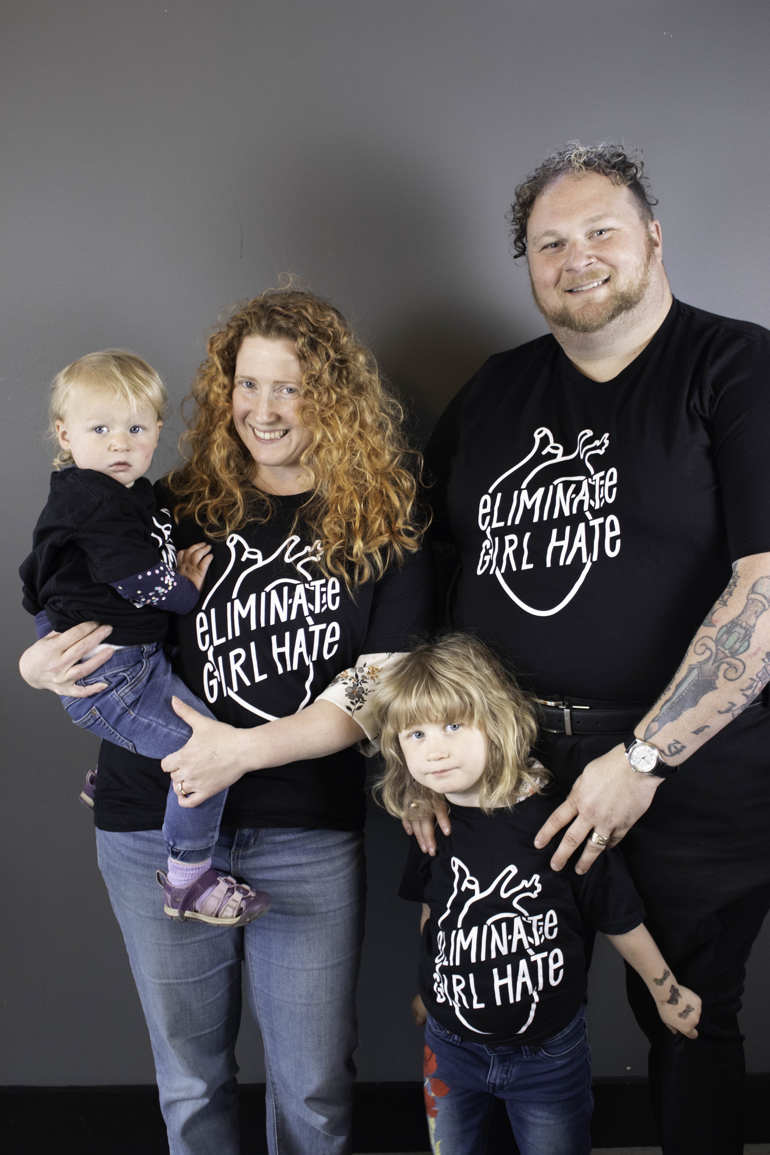 Father and mother with two young children wearing the black unisex Eliminate Girl t-shirt