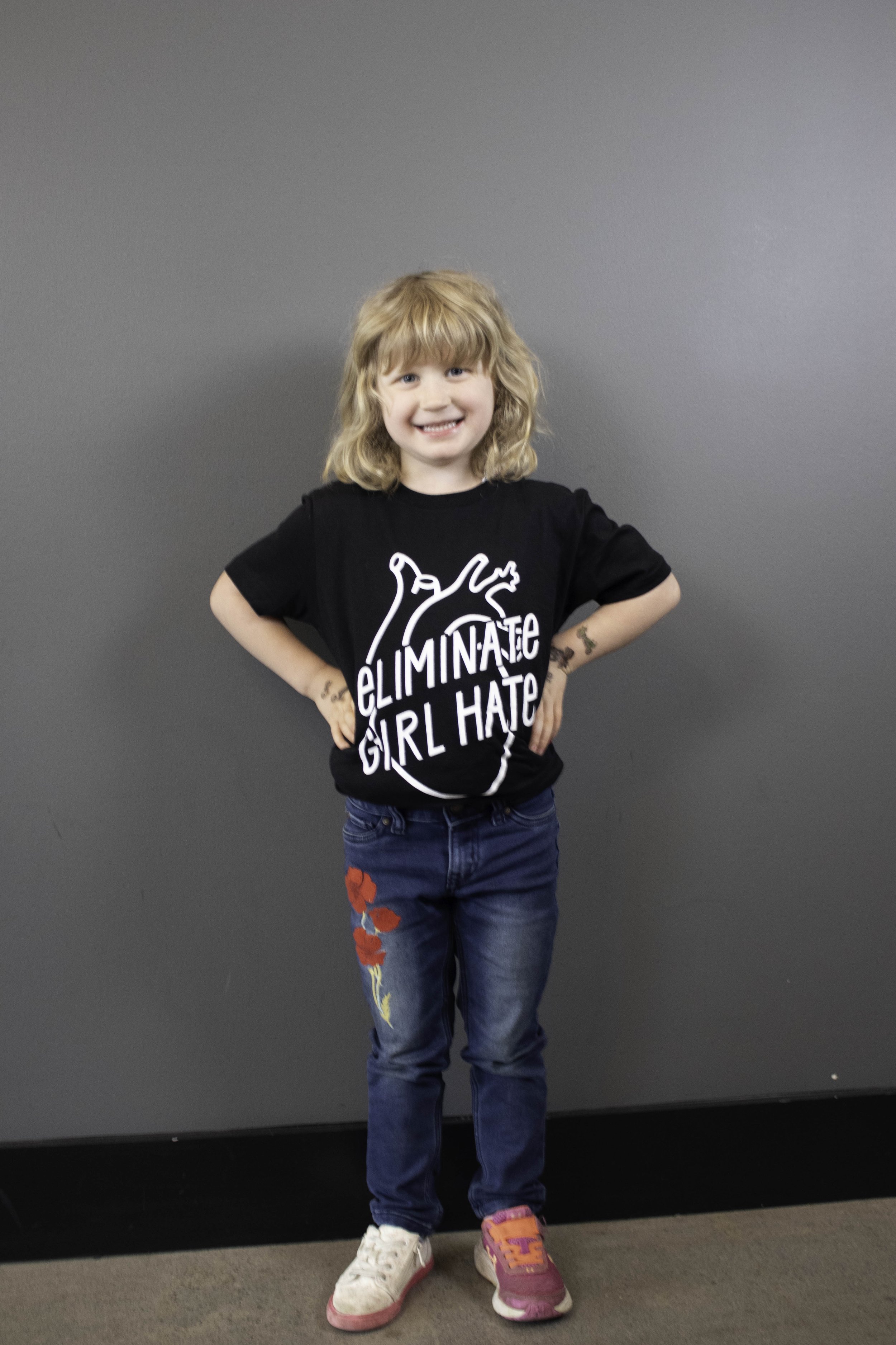 Young child wearing the black unisex Eliminate Girl t-shirt