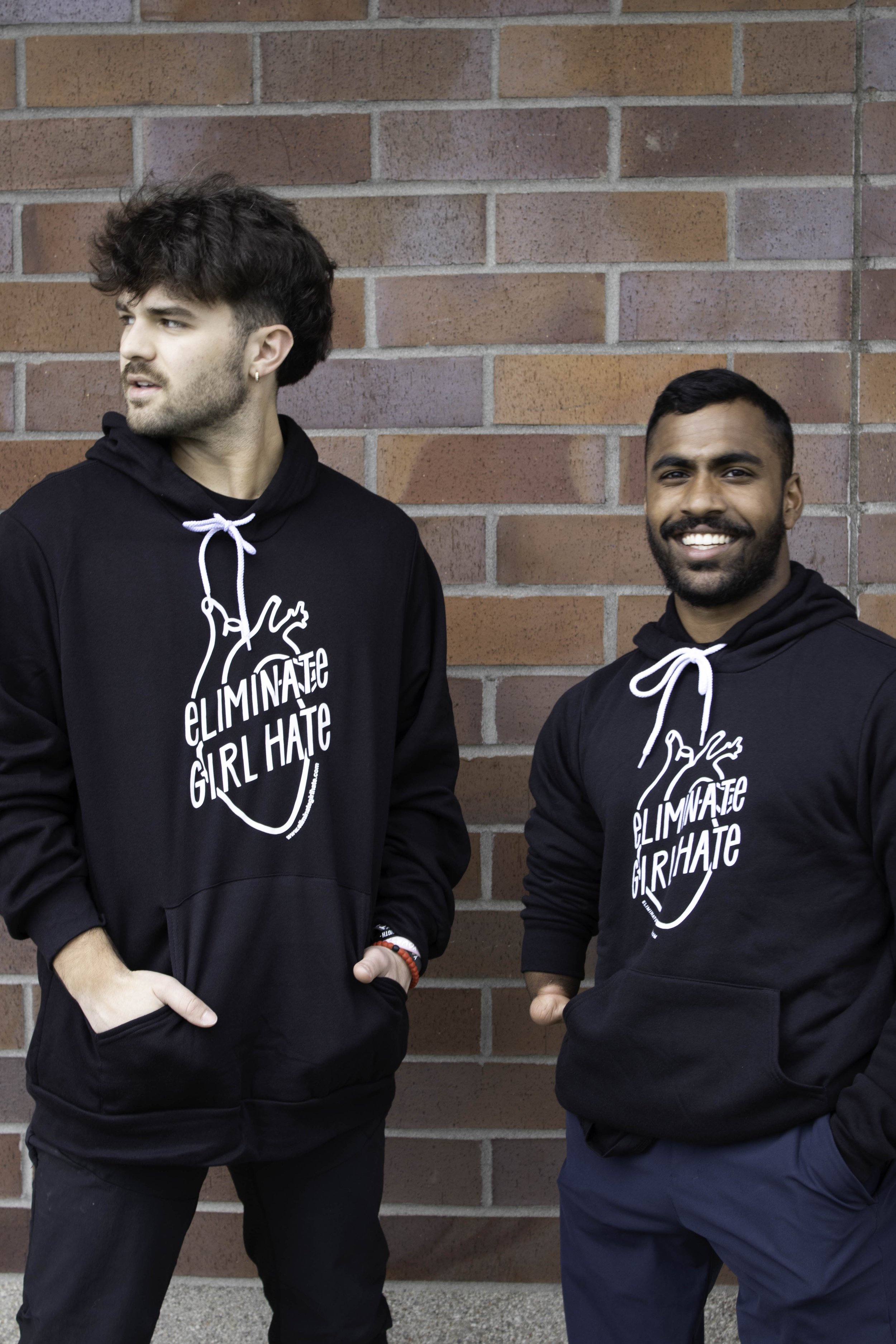 Two young college men smiling and wearing the Eliminate Girl Hate unisex hoodie