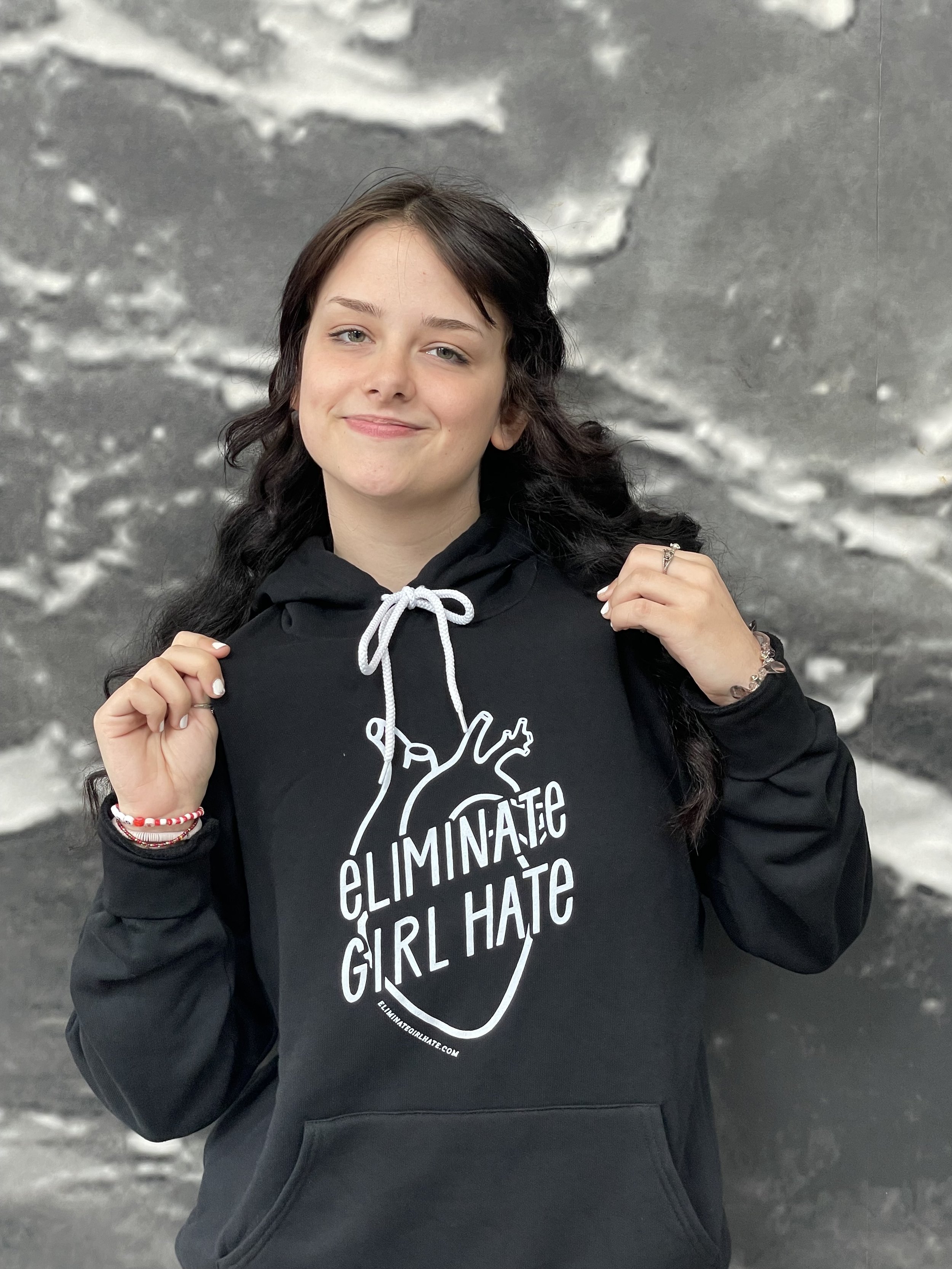 Young woman smiling and wearing the Eliminate Girl Hate unisex hoodie